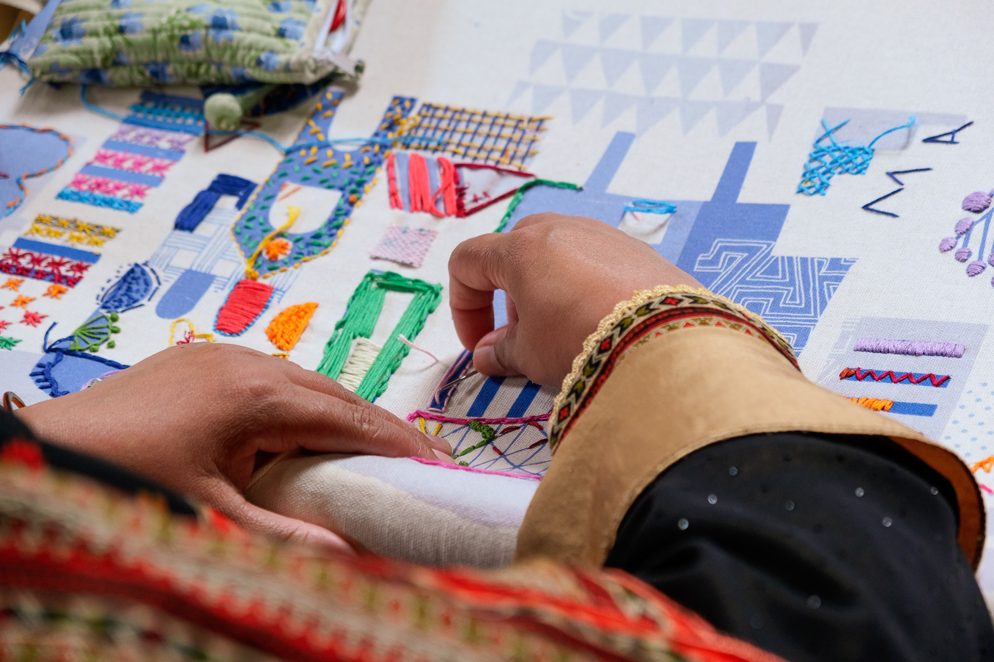 Hands stitch on fabric, adding to the growing colour of the artwork.