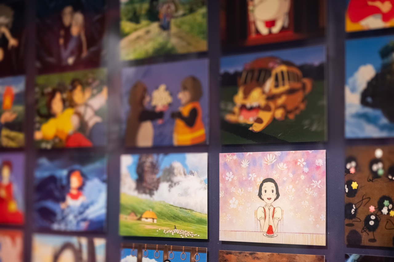 A wall display featuring a collage of vibrant animated scenes, including cartoon characters, nature landscapes, and fantasy elements, with one central image showing a smiling girl surrounded by white flowers.
