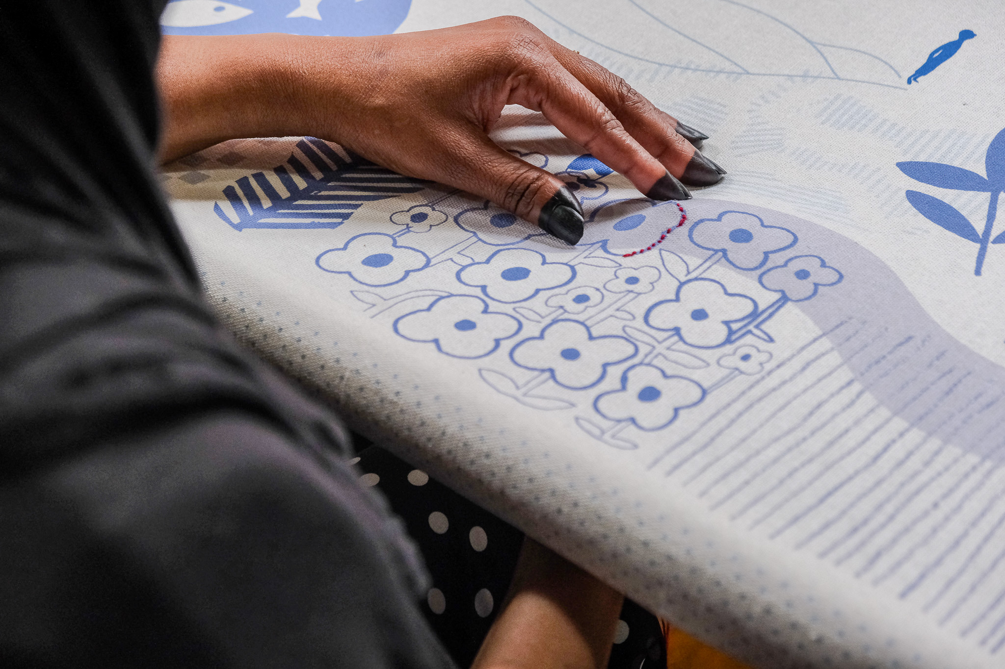 A person touches a patterned fabric featuring blue floral designs.
