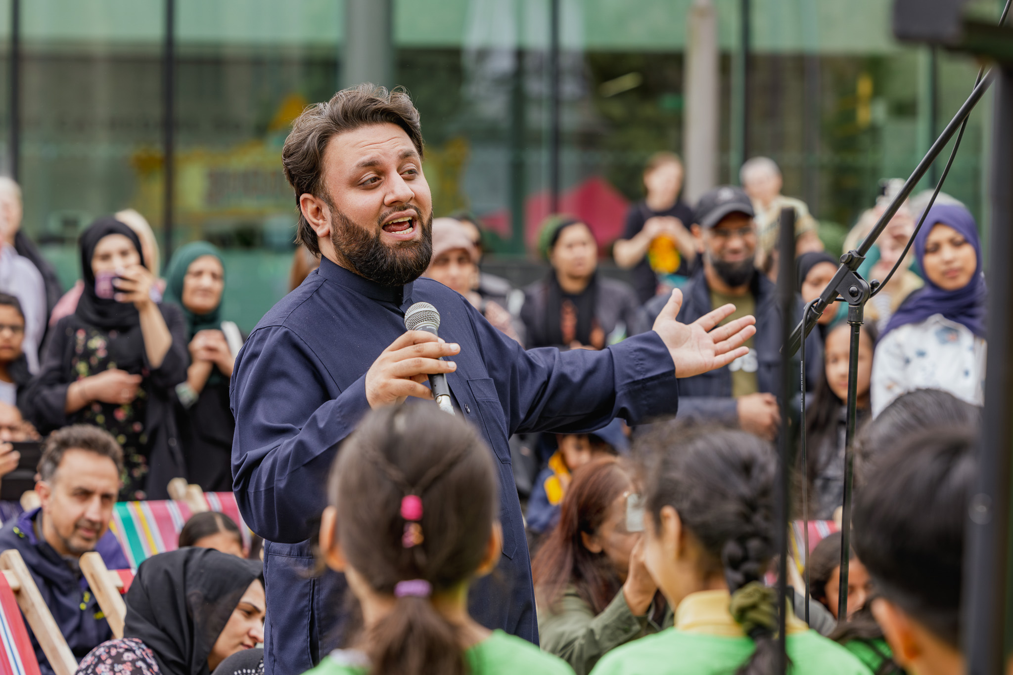 A man in a blue shirt sings to a large crowd with a microphone.