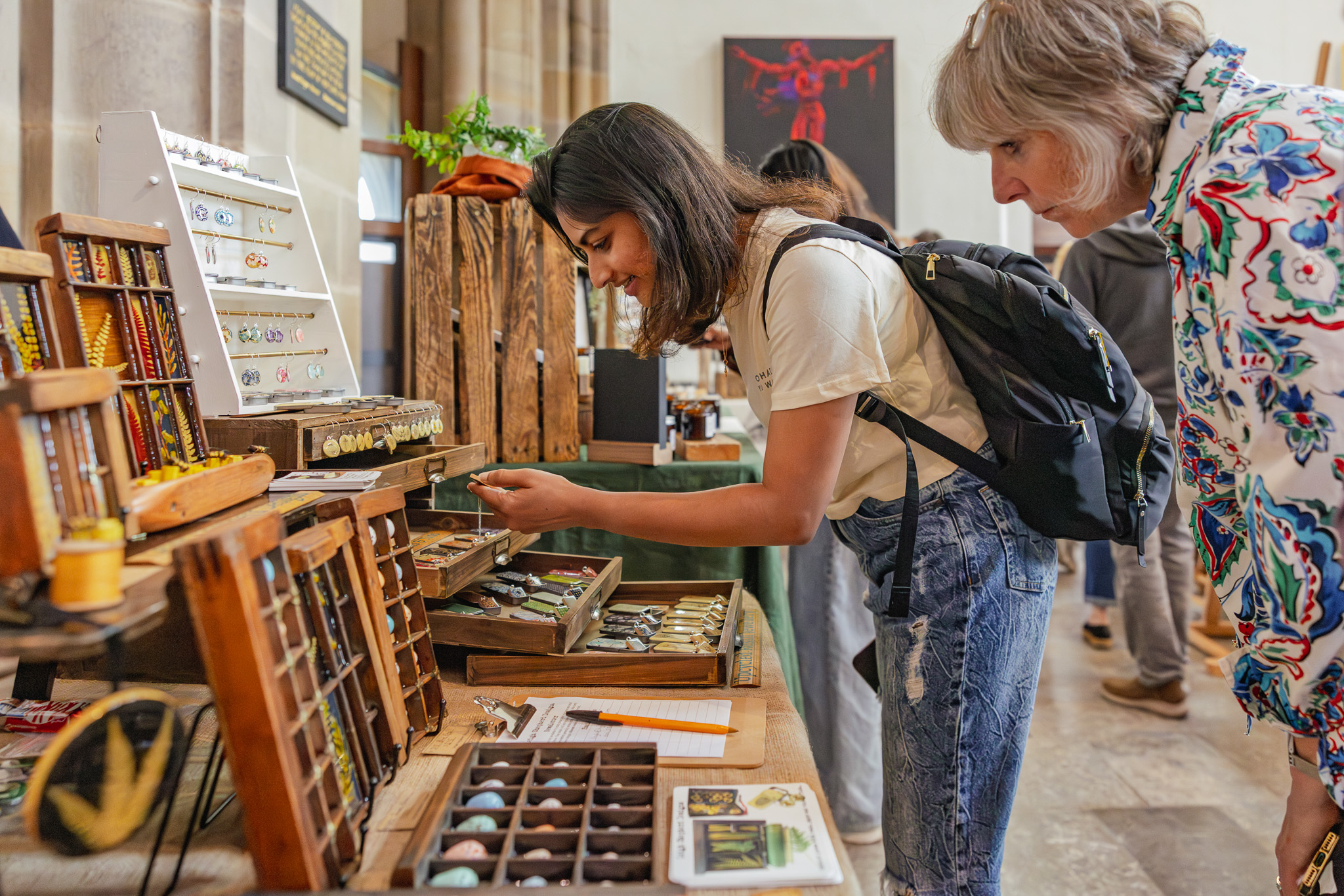 Two women browse handmade jewellery at a makers market.