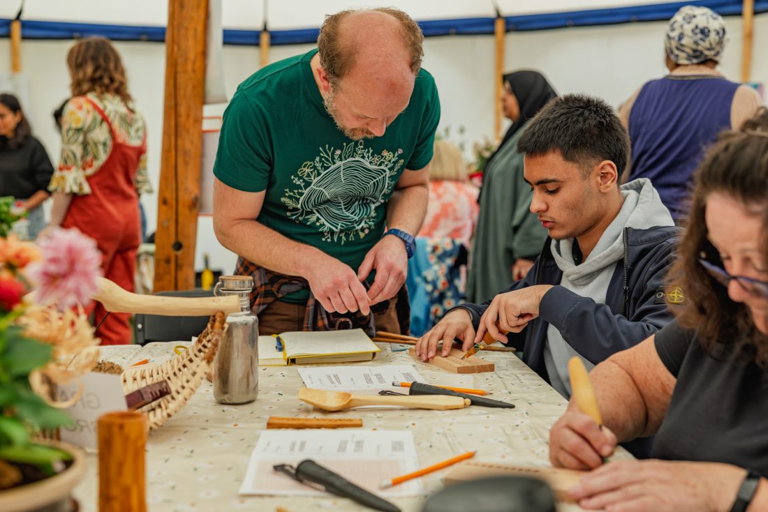 People engage in a wood carving workshop, focusing intently on their projects at a table filled with tools and materials.