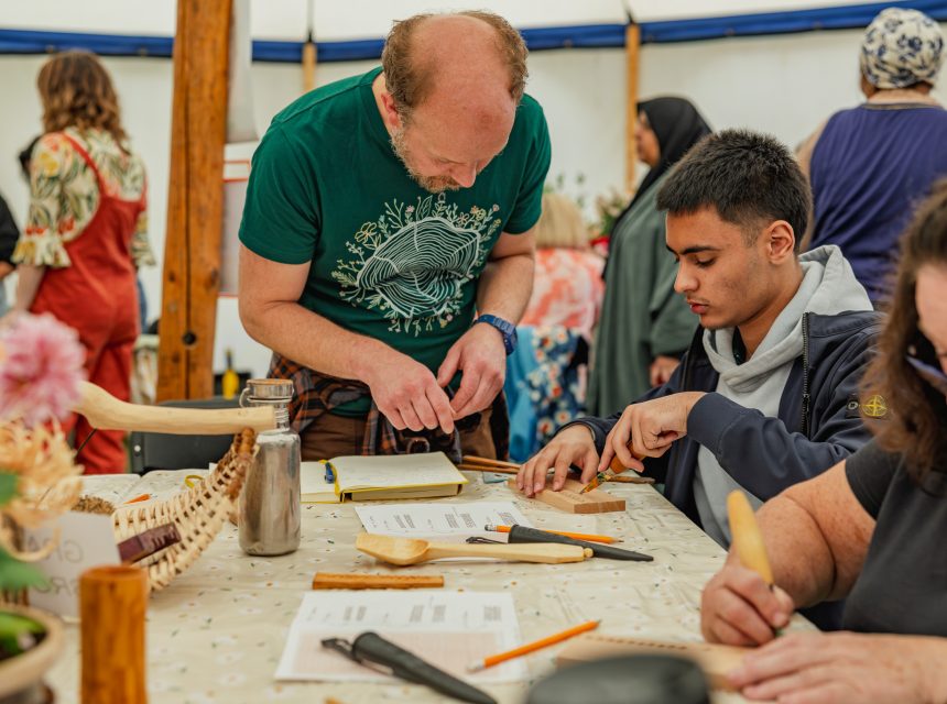 People engage in a wood carving workshop, focusing intently on their projects at a table filled with tools and materials.