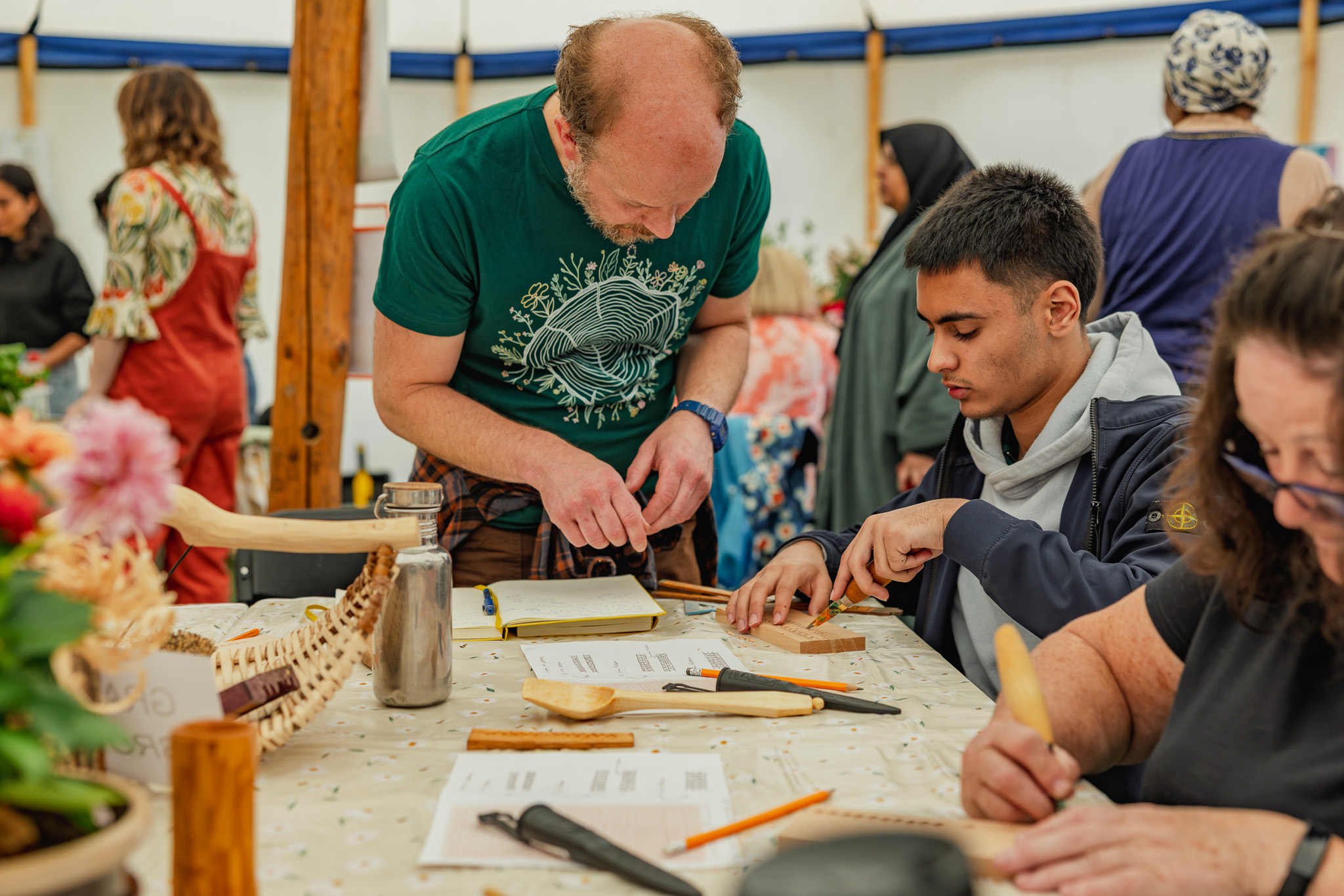 People engage in a wood carving workshop, focusing intently on their projects at a table filled with tools and materials.