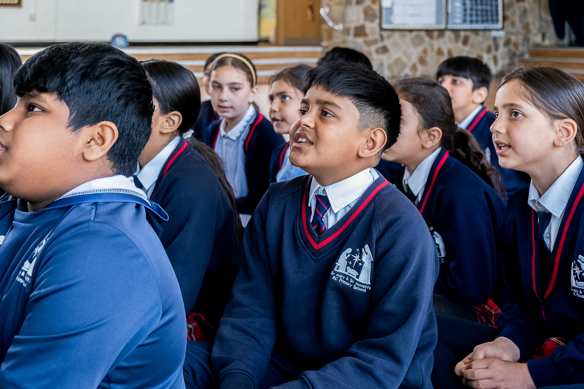 Group of children in school uniforms singing indoors.