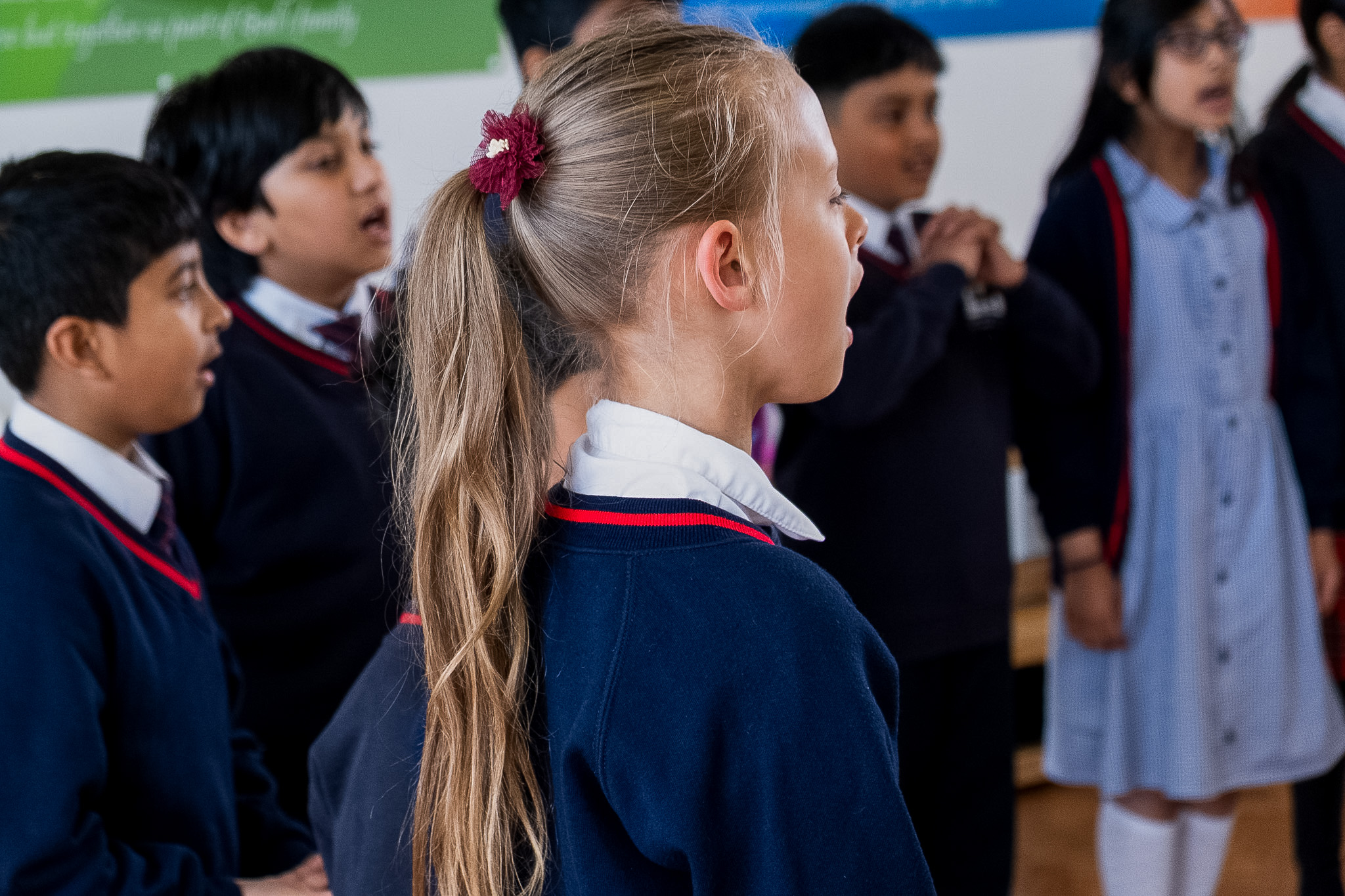 Group of children in school uniforms singing indoors.