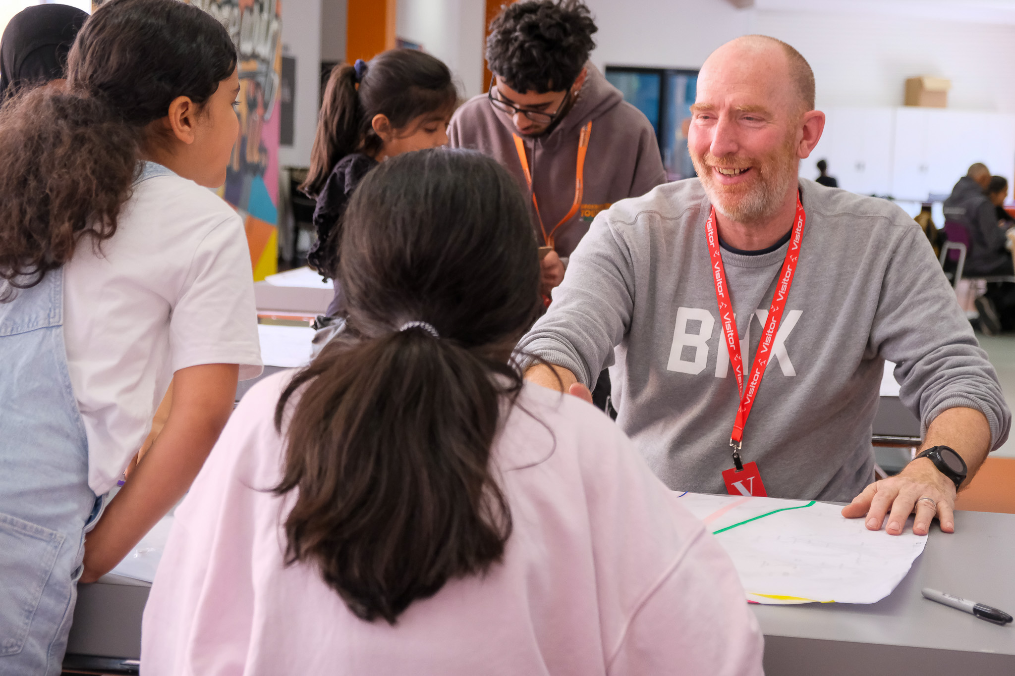 A smiling artist engages with a group of children around a table.