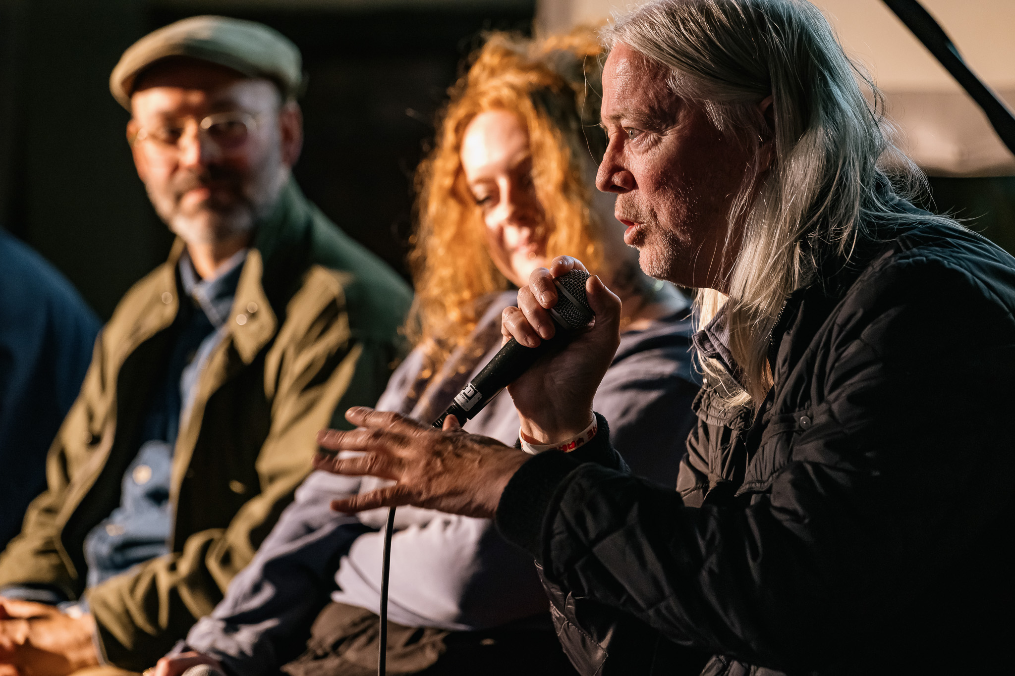 The people seated on a dimly lit stage, engaging in a panel discussion.