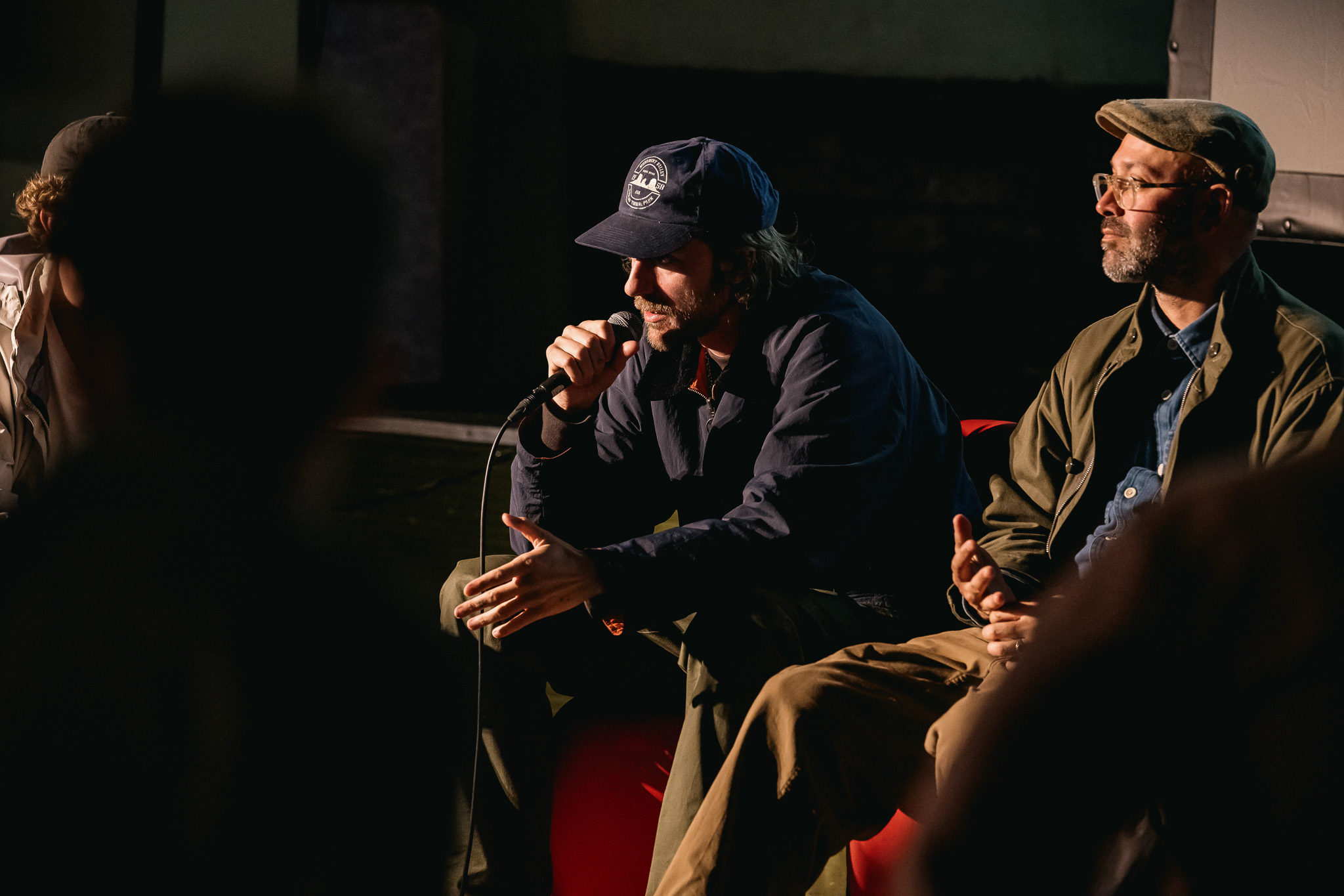 Two people seated on a dimly lit stage, engaging in a panel discussion.