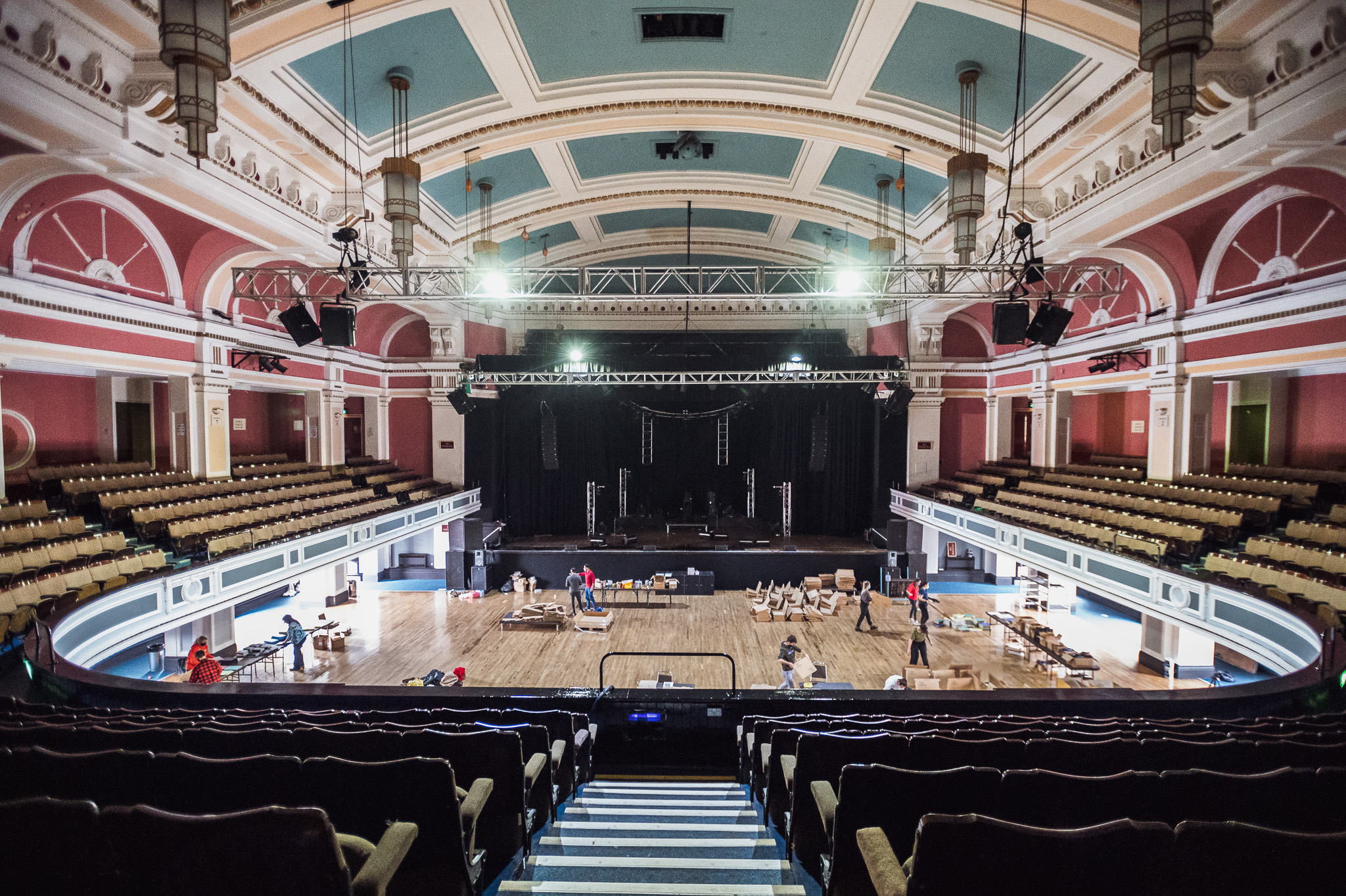 An ornate theatre with a large stage, curved balcony seating, and decorative ceiling, as people pack boxes on the floor.