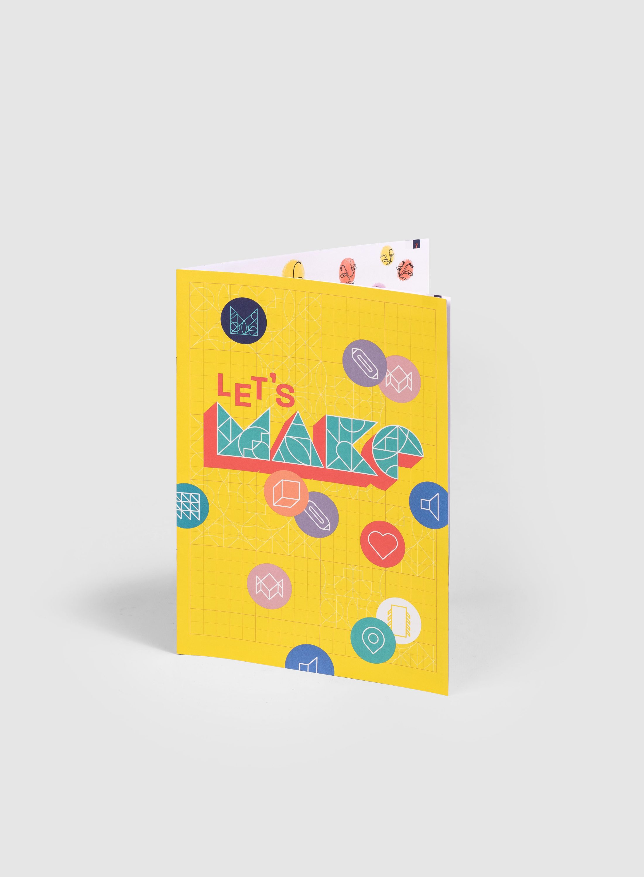 A colourful greeting card with a yellow cover featuring the words LET'S MAKE in bold letters and various icons, such as chat bubbles, hearts, and location pins, scattered around the front.