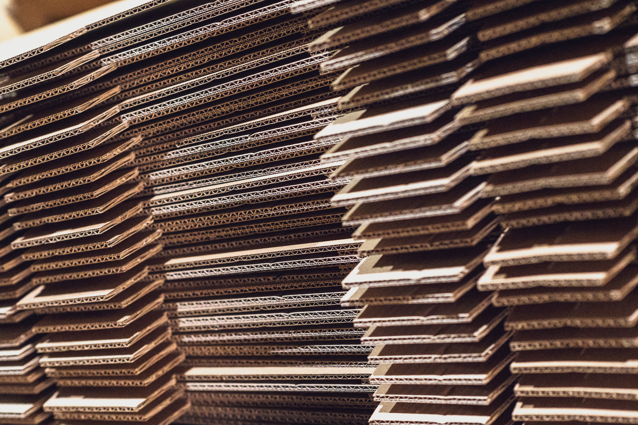 Stacks of corrugated cardboard sheets arranged closely together, showing the layered and textured edges in a warehouse or packaging facility.