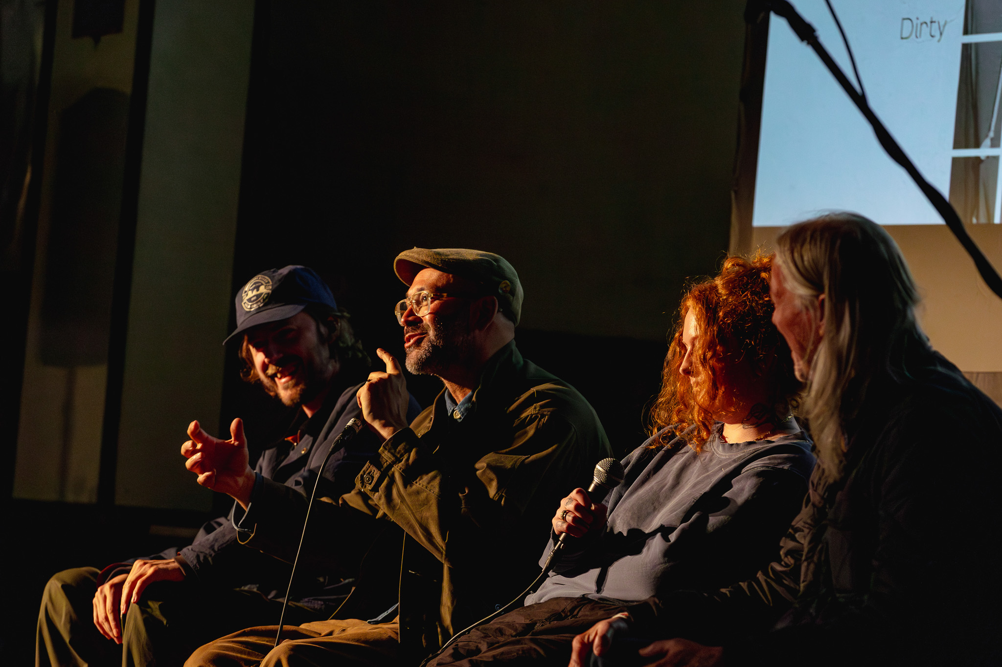 Four people seated on a dimly lit stage, engaging in a panel discussion.