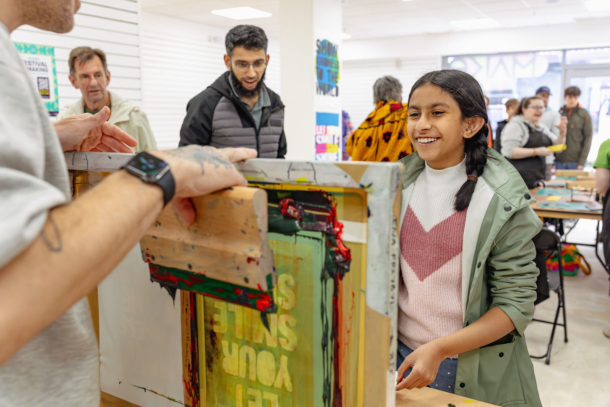 A group of people engaged in a screen printing activity, with one girl smiling as she operates a screen printing frame, while others observe and participate around her.