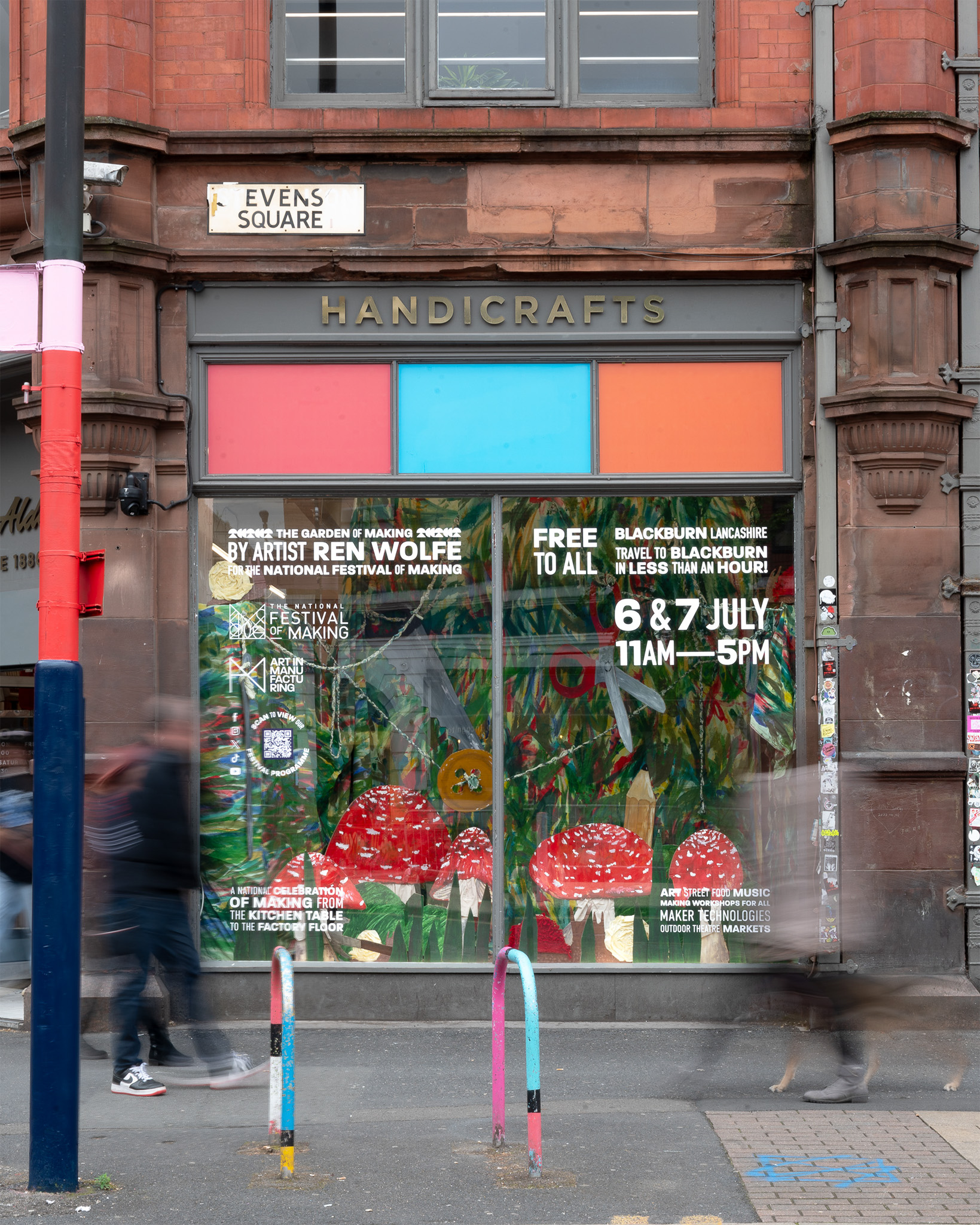 A shopfront with “HANDICRAFTS” above the window displays colourful posters for an art event with red spotted mushrooms, dates 6 & 7 July, and event details. Blurred pedestrians pass by on the pavement.