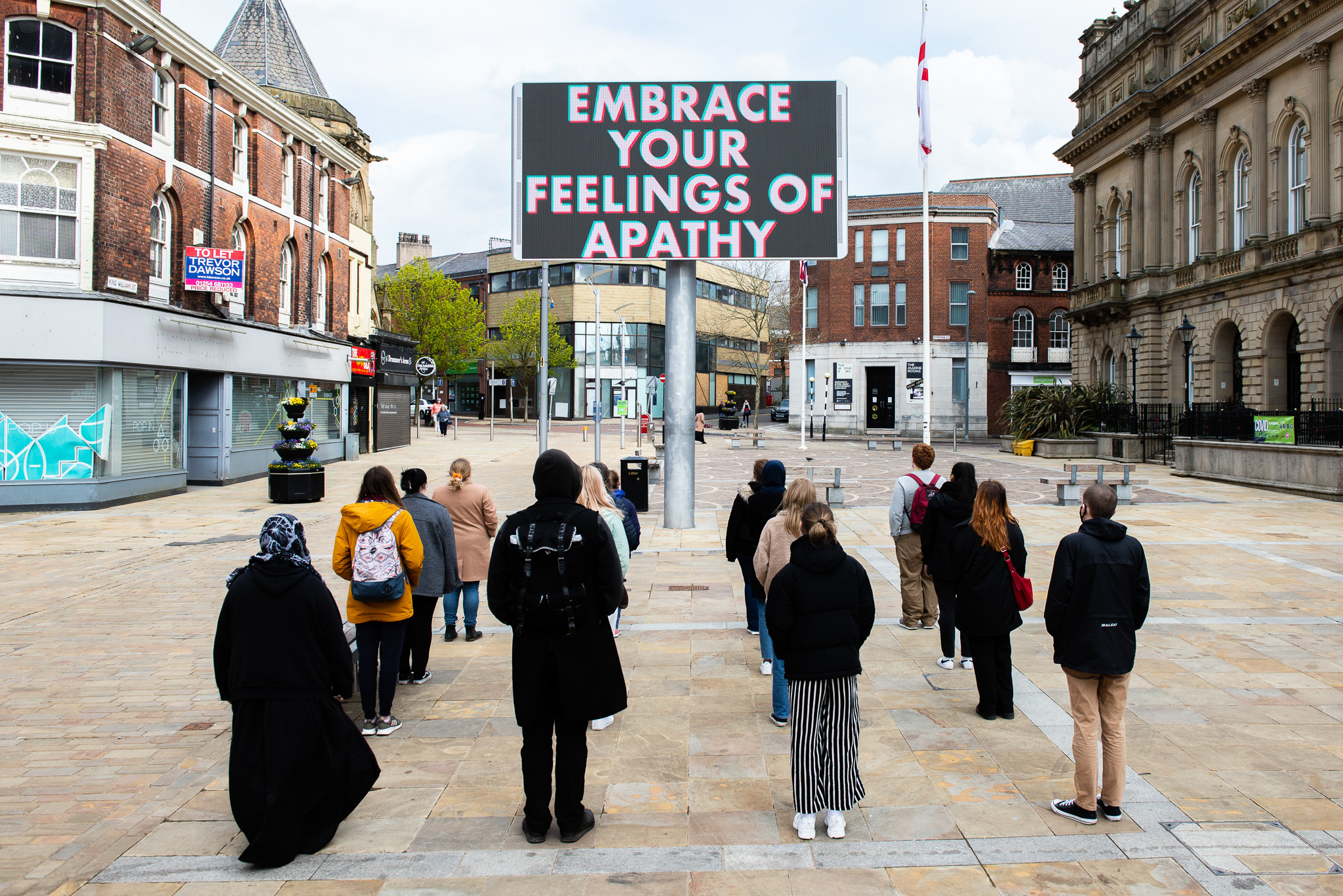 A group of people standing in a square with a large sign that reads 