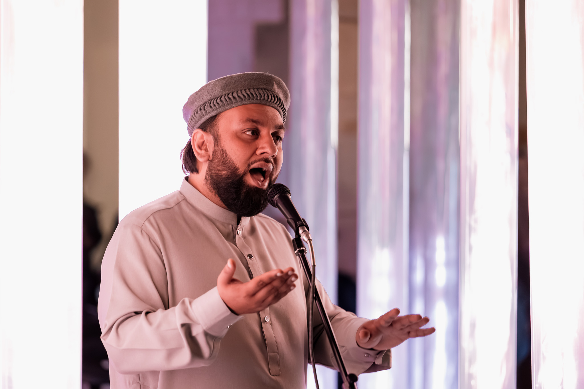 A man in traditional attire sings into a microphone on stage, surrounded by tall, glowing vertical light columns.