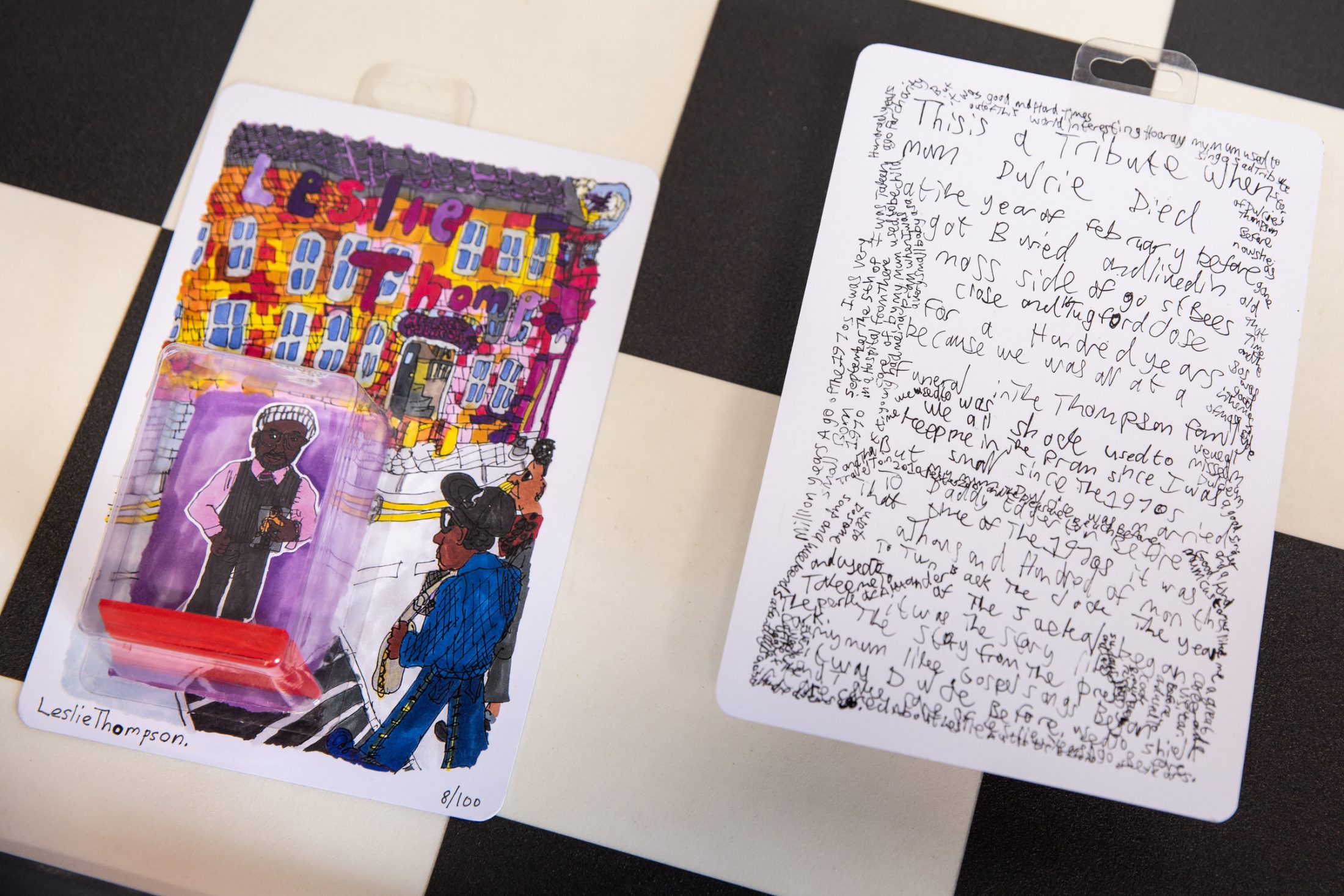 Art piece with a colorful illustration of people and vibrant text, alongside a black-and-white handwritten note on a checkerboard table.
