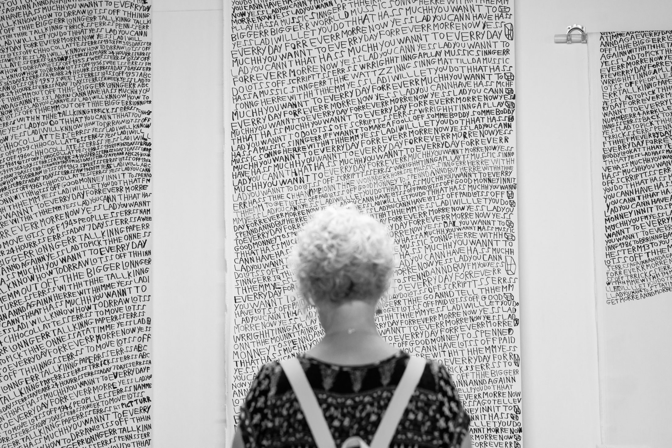 A person with curly hair is viewed from behind, observing large black-and-white text panels in an art gallery.