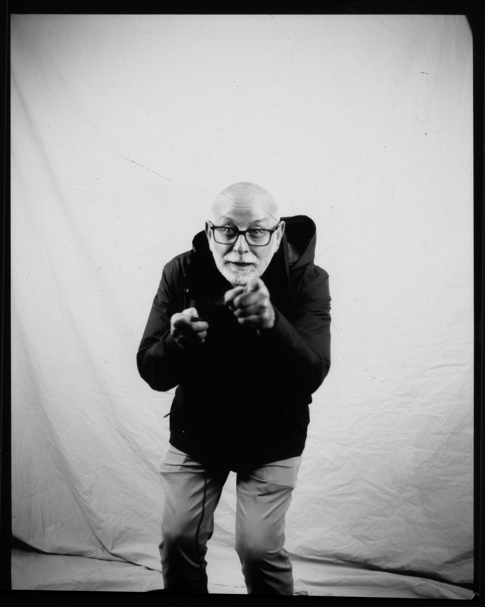 Black and white image of an adult in front of a white sheet leaning forward, hands pointed in front.