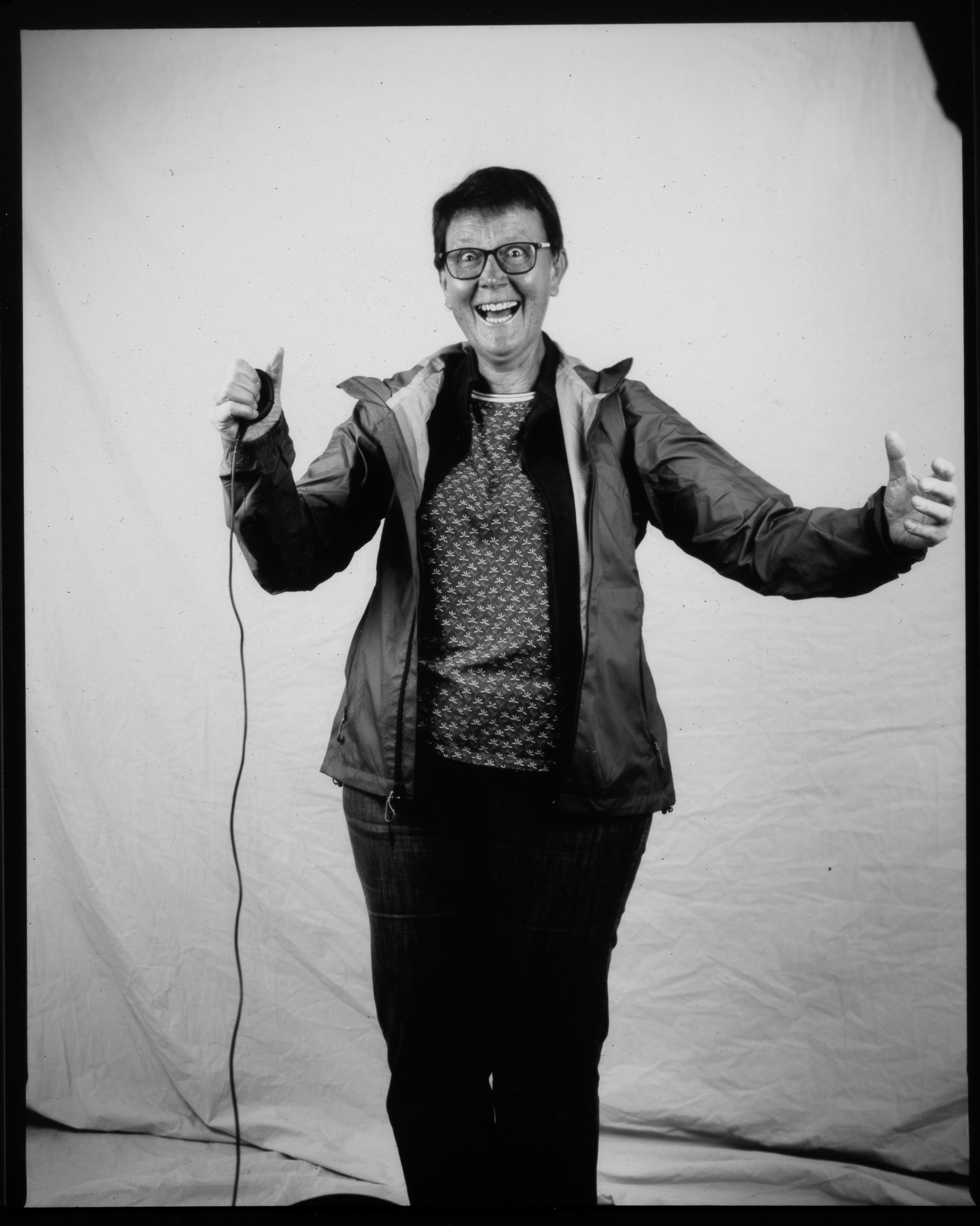 Black and white image of an adult stood smiling with arms outstretched pressing a remote with a wire trailing.