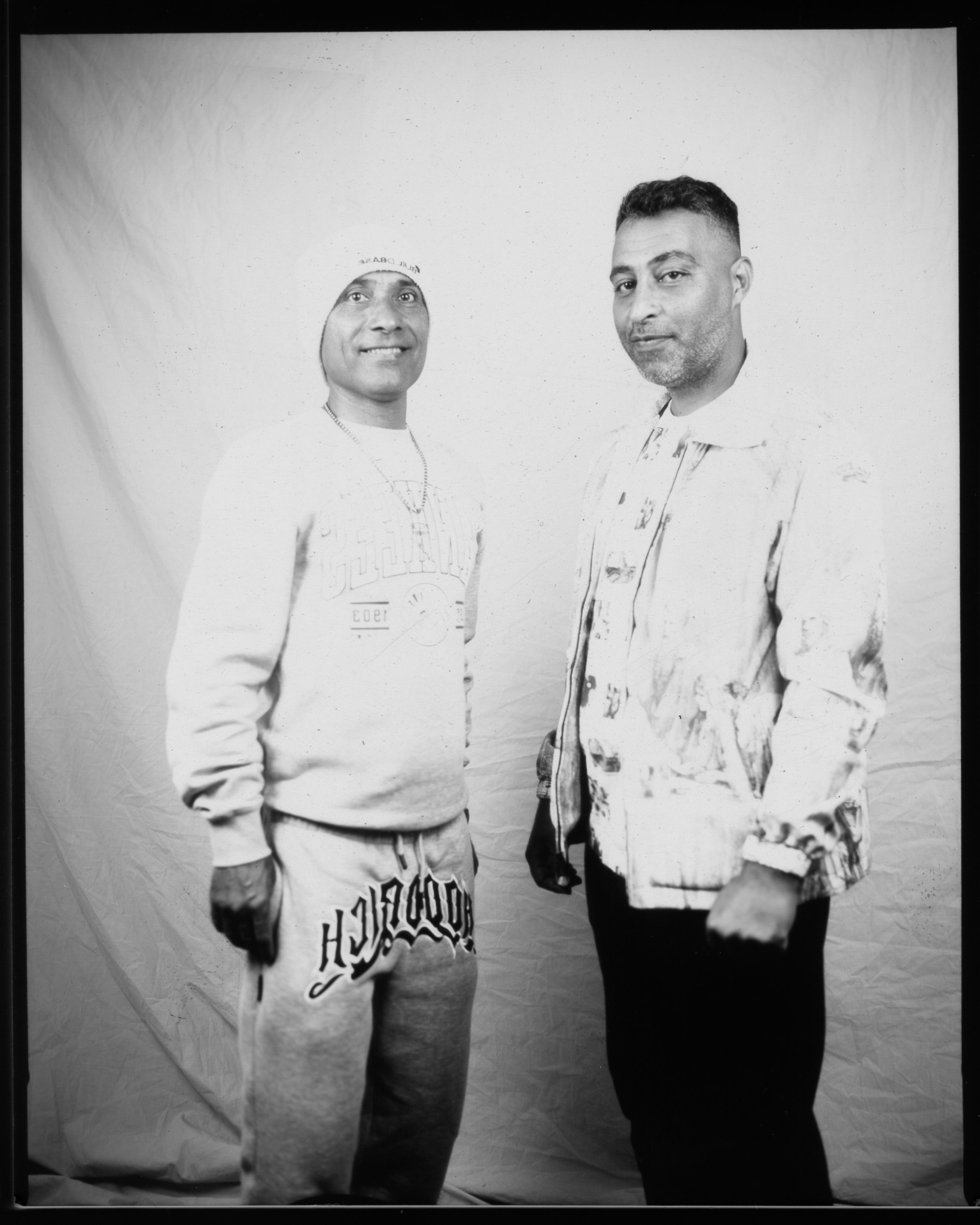 A black and white image of two adults stood smiling in front of a white sheet.
