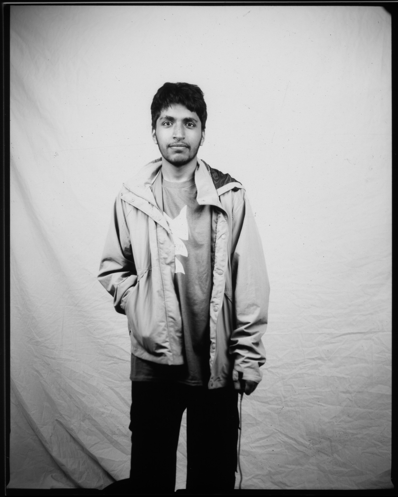 A black and white image of a standing adult in front of a white sheet pressing a remote, a wire trailing to the ground.