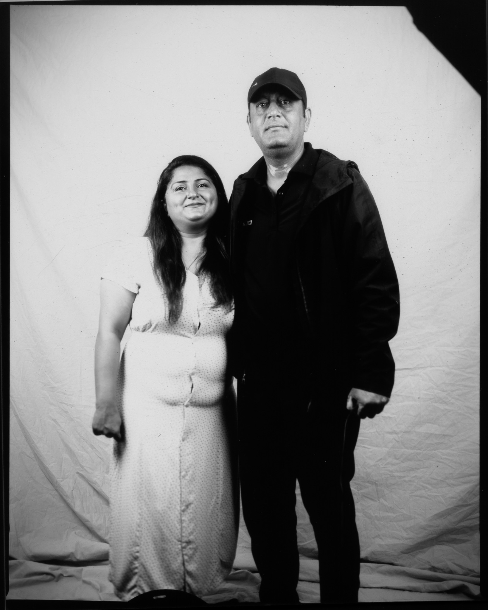 A black and white image of two adults stood closely together smiling in front of a white sheet.