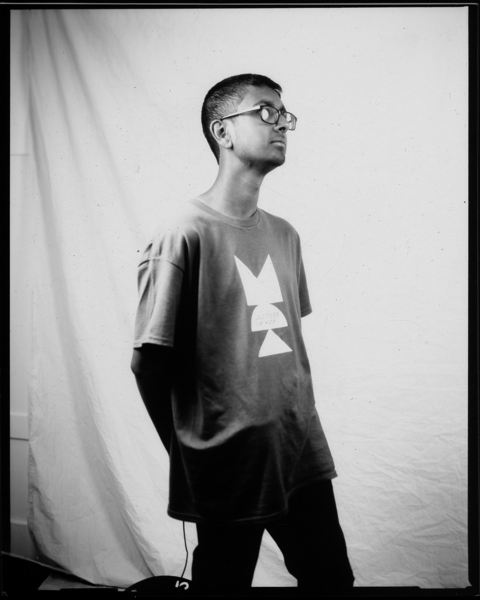 A black and white image of an adult turned looking away. They are stood in front of a white sheet.