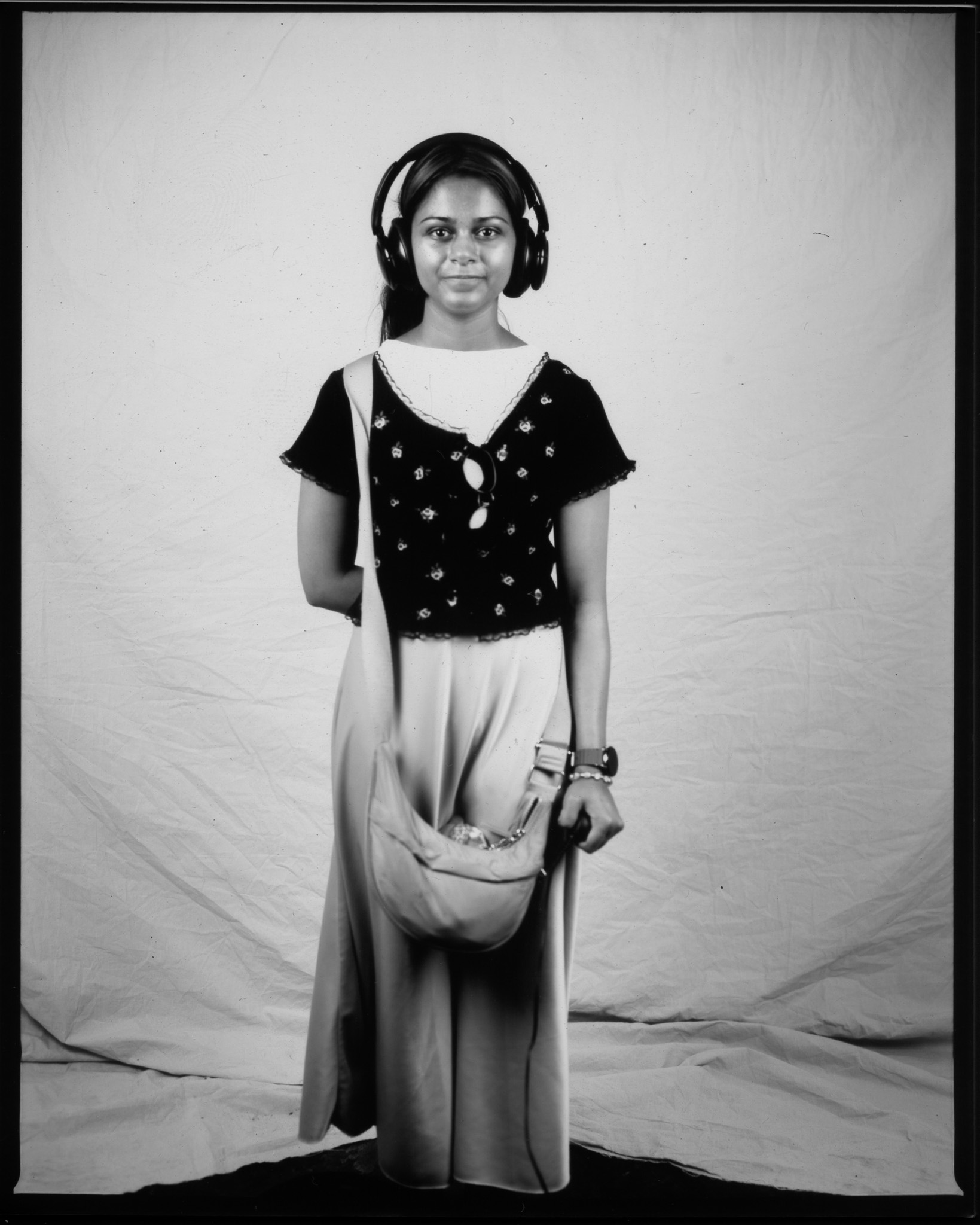 Black and white image of a young adult wearing large headphones stood smiling in front of a white sheet.