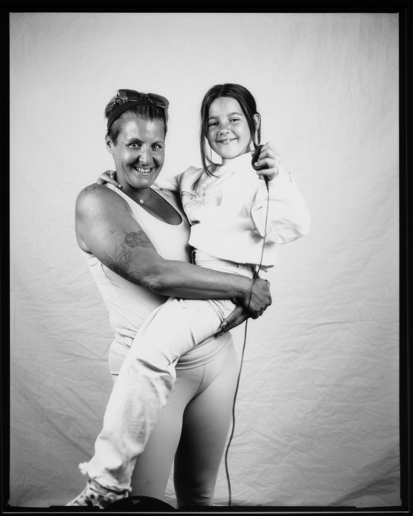 A smiling woman holds a young girl in her arms against a plain backdrop in a black and white photo.