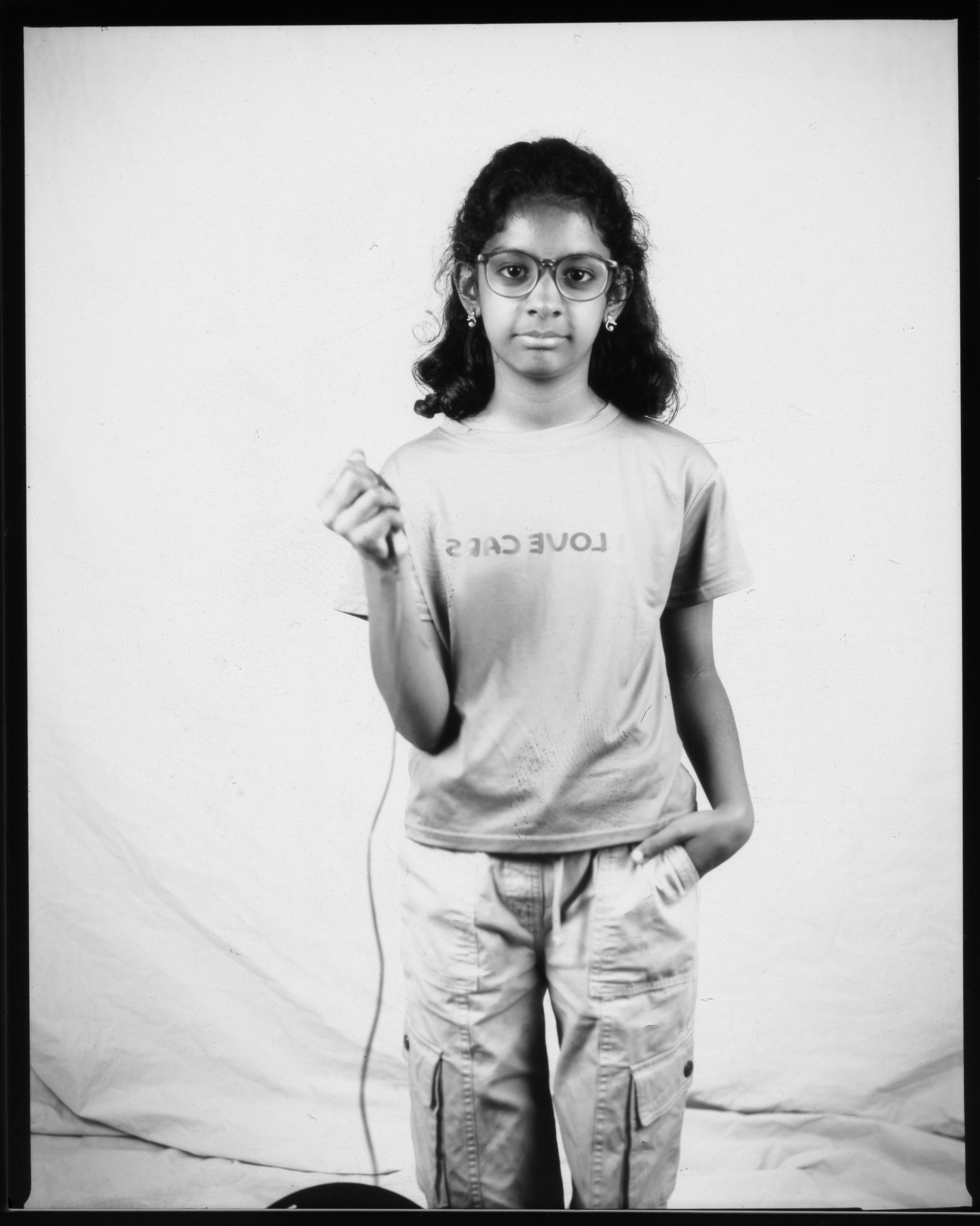 Black and white image of a child smiling in front of a white sheet, pressing a remote with a wire trailing.