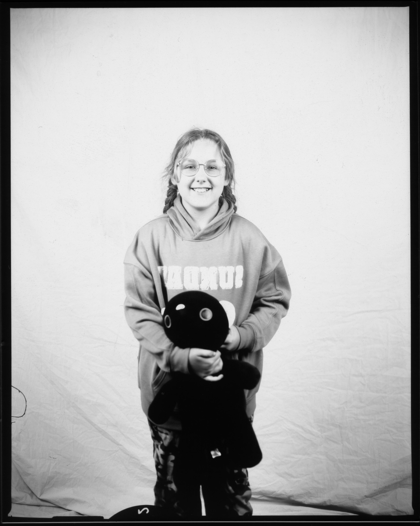 A black and white image of a young person smiling in front of a white sheet holding a teddy.
