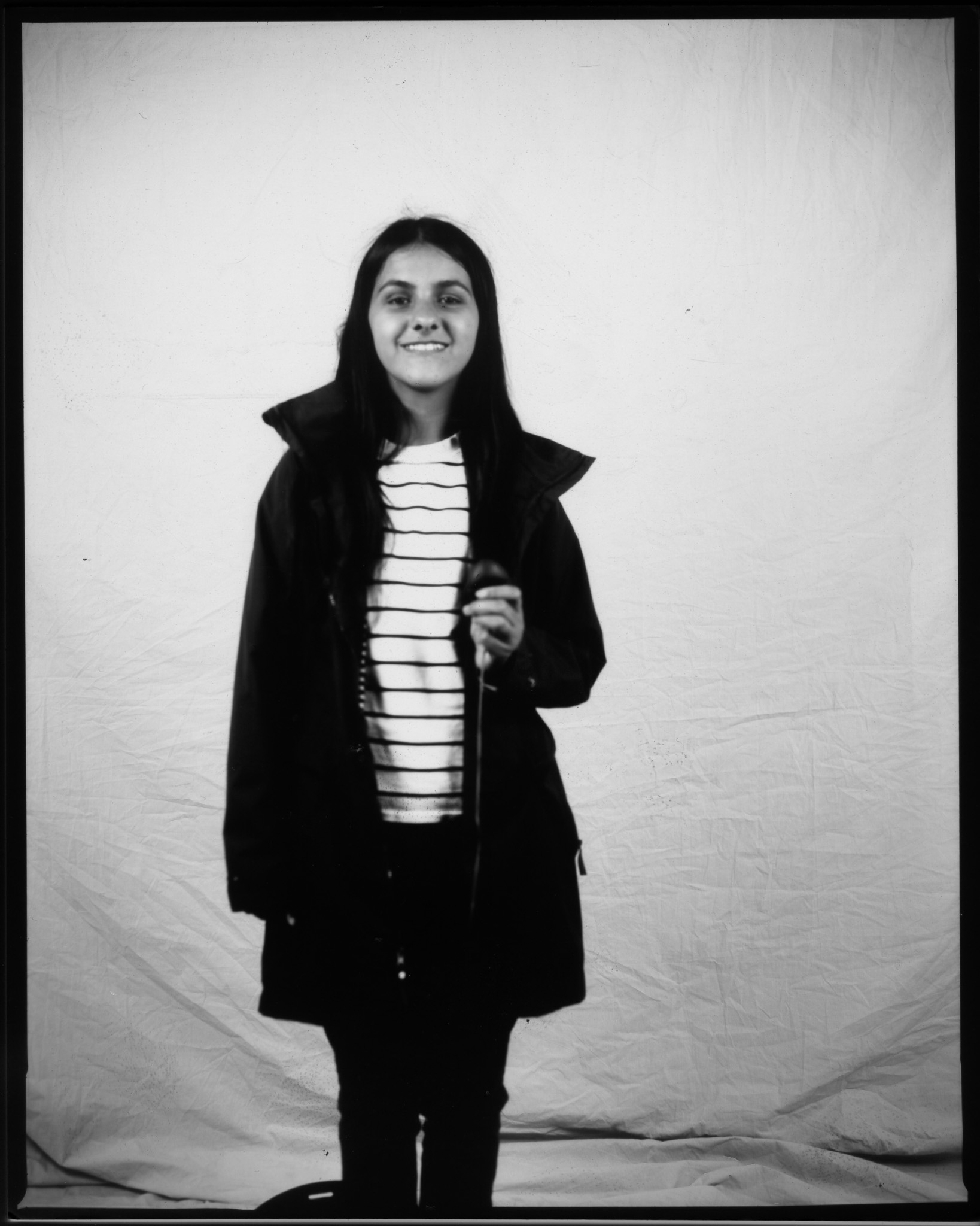 Black and white image of a teenager smiling in front of a white sheet, pressing a remote with a wire trailing.
