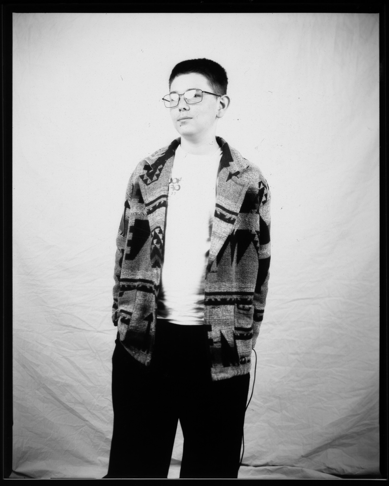 A person in glasses and a patterned sweater poses confidently against a plain backdrop, in a black and white photo.