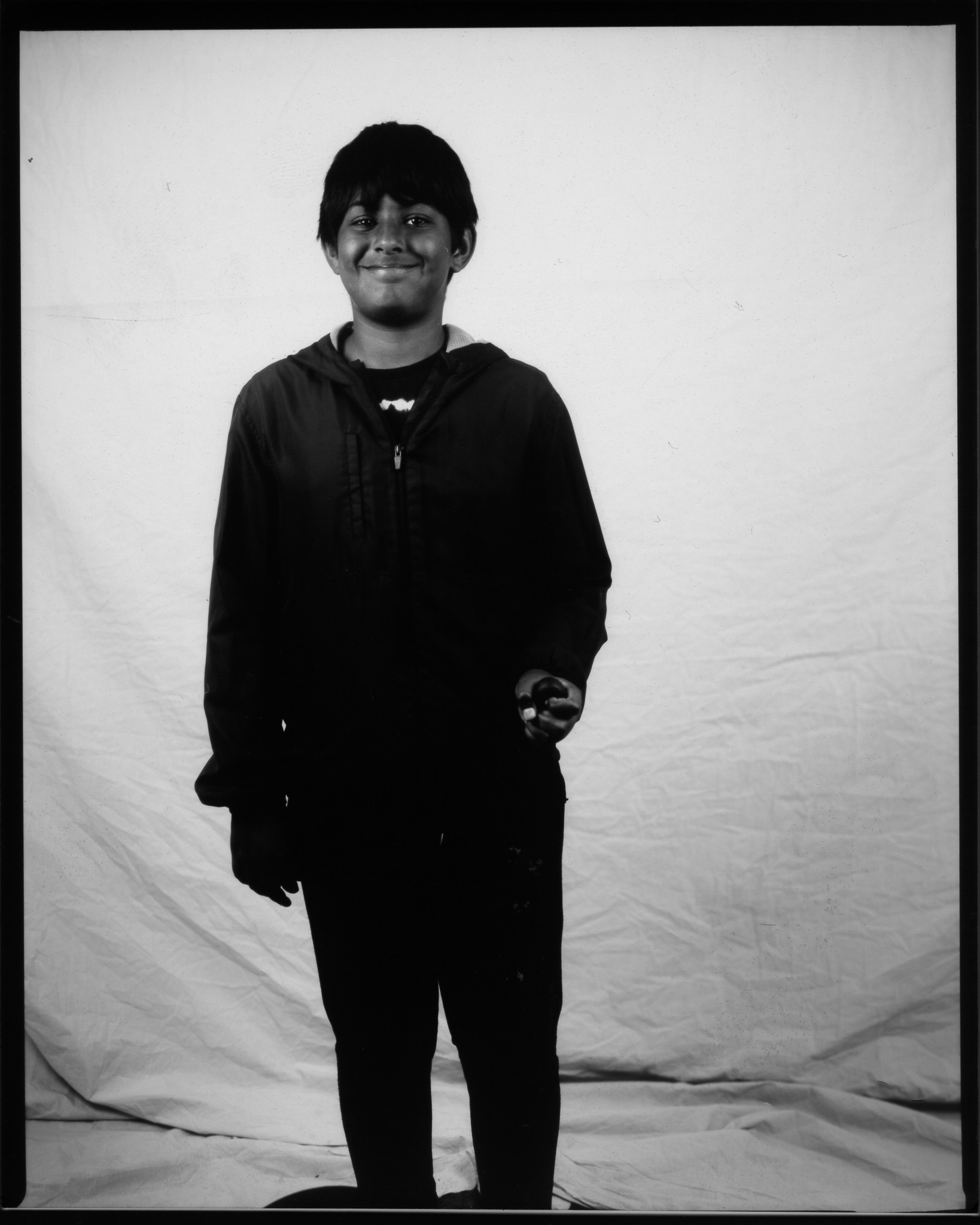 Child smiling and posing wearing a black hoodie in a black and white photo.