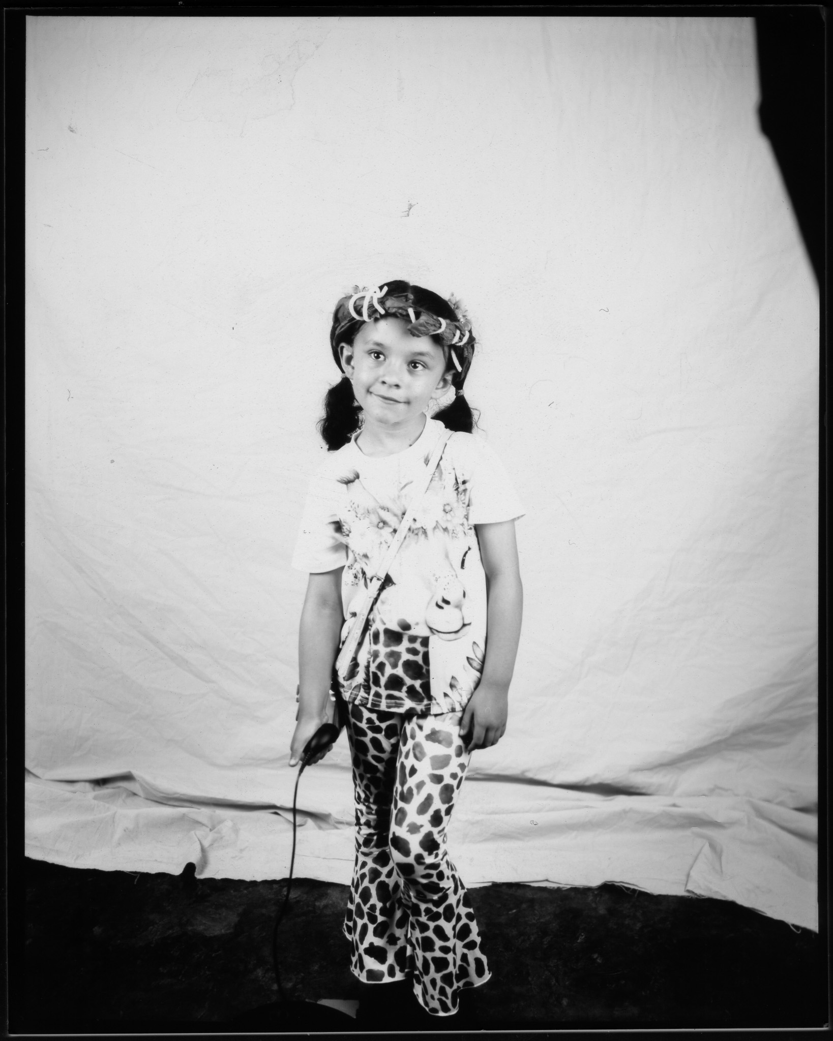 Child with pigtails wearing animal print flared trousers, smiling and posing in a black and white photo.