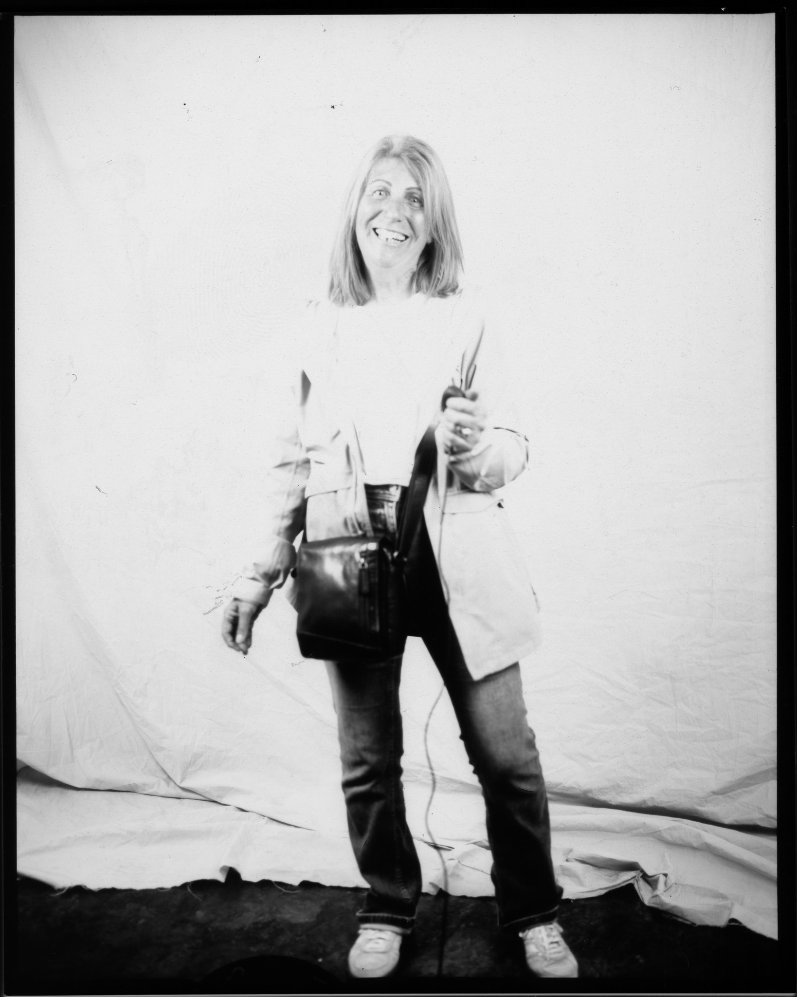 Adult with mid-length hair wearing jeans and a light jacket, smiling and posing in a black and white photo.