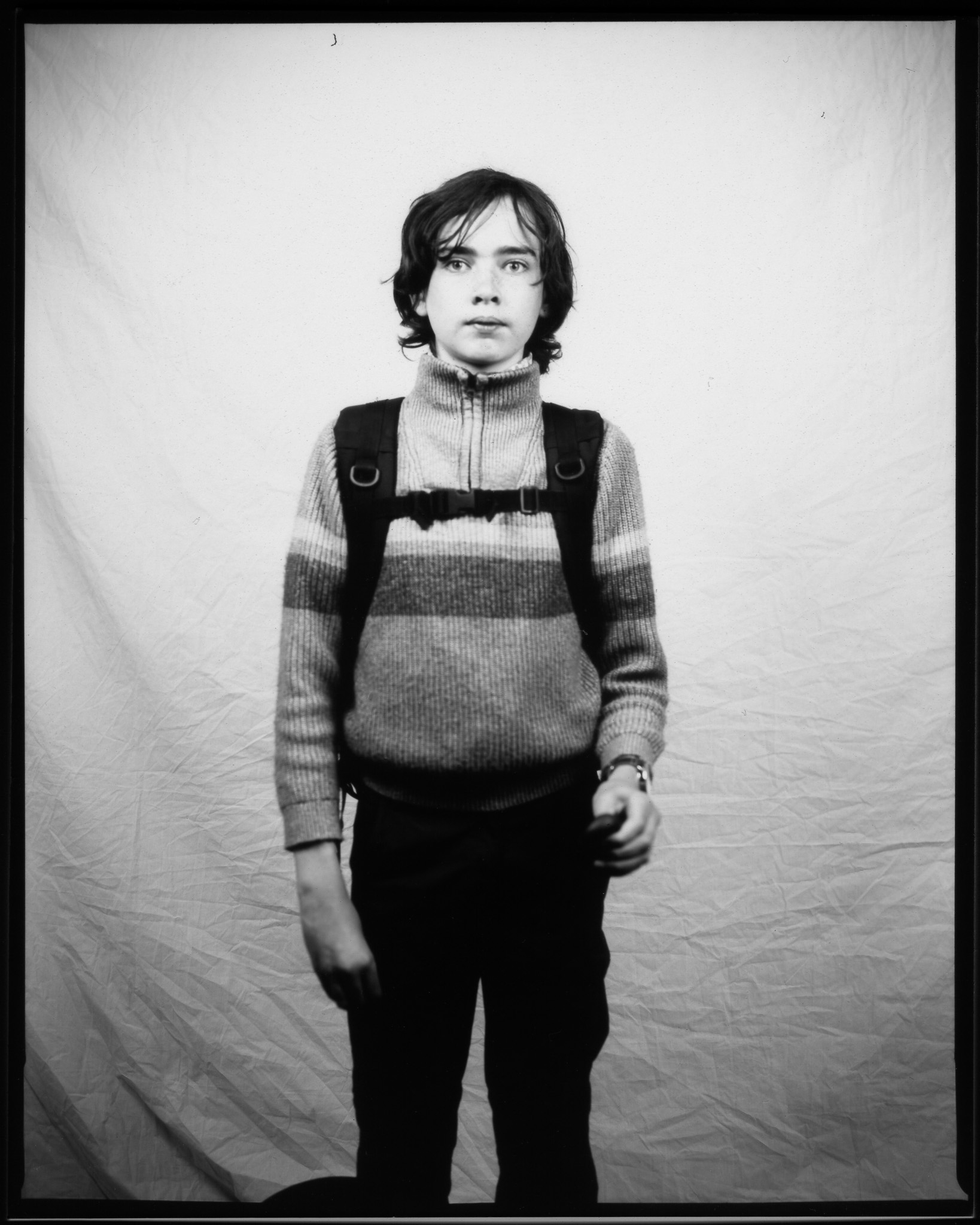 A black and white image of a standing teenager in front of a white sheet while pressing a remote shutter release button.