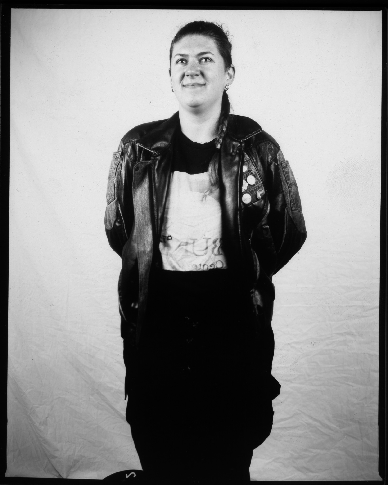 A black and white image of a standing adult smiling in front of a white sheet.