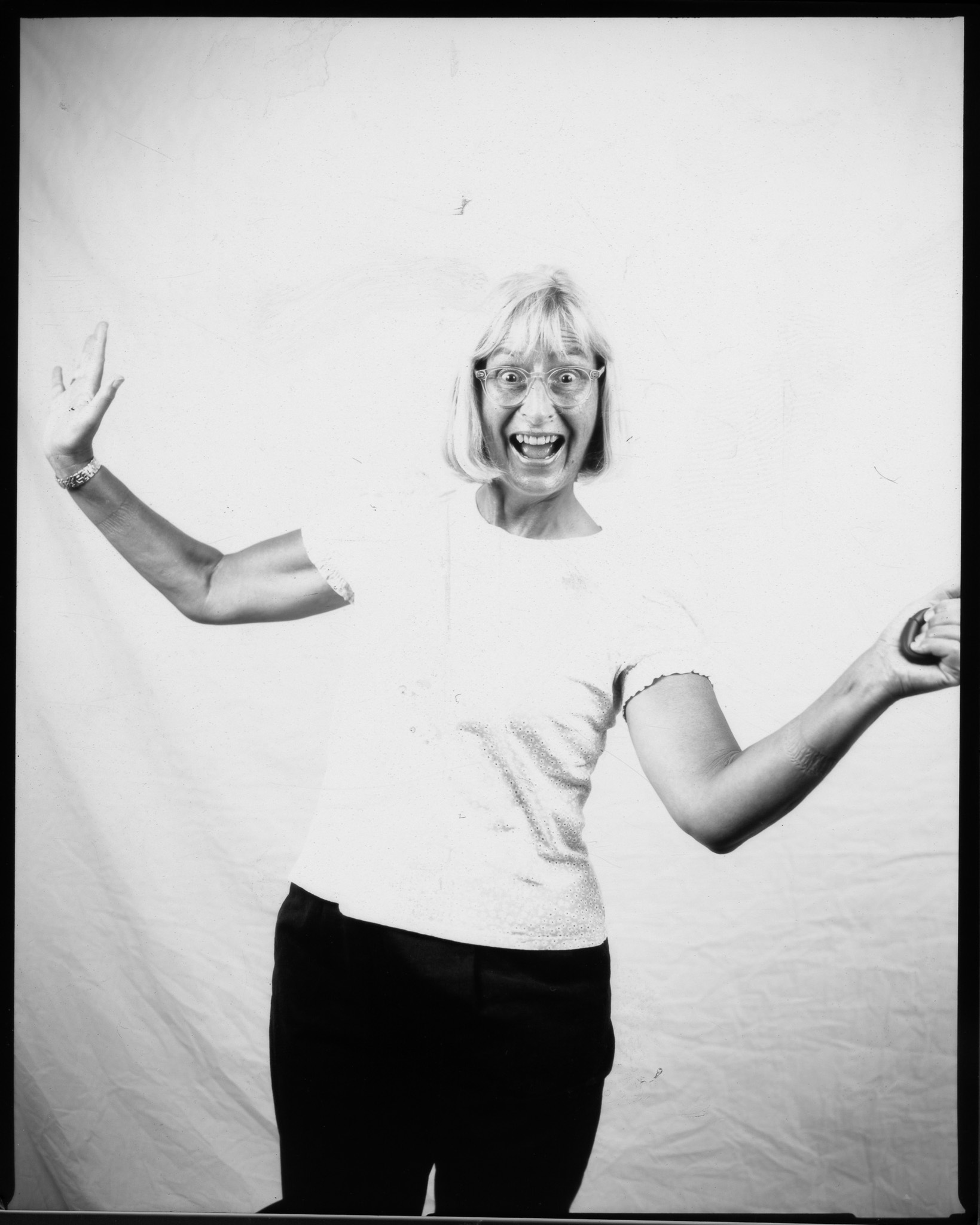 Black and white image of a smiling adult in front of a white sheet, arms outstretched pressing a remote button.