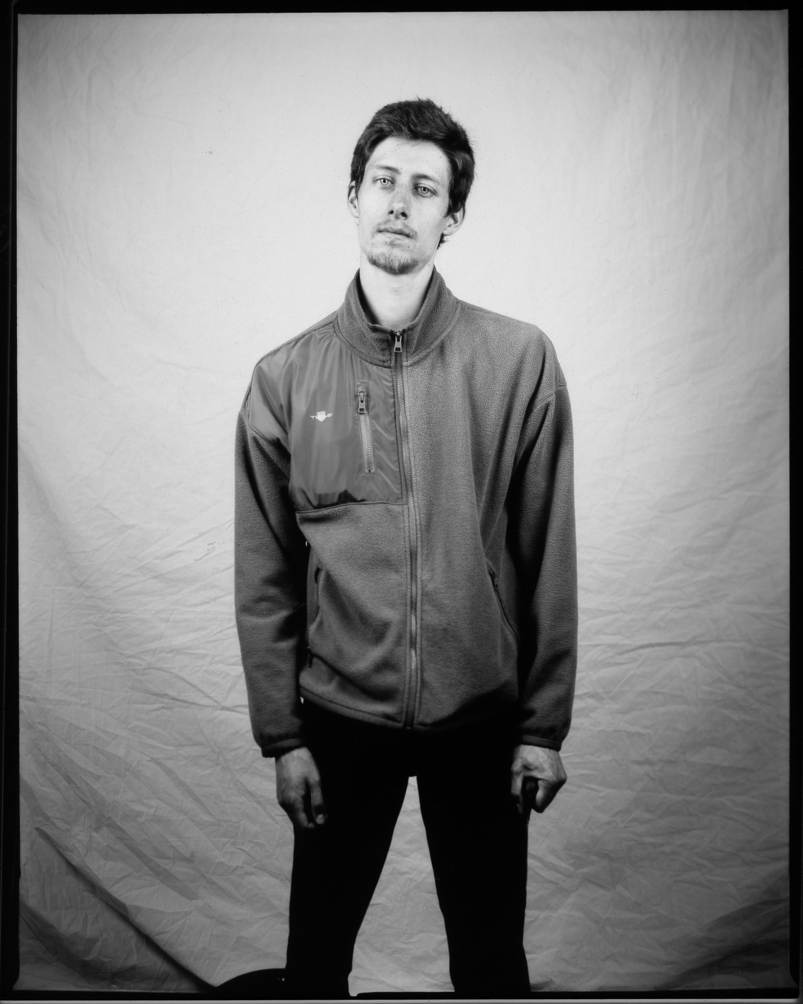 A black and white image of a standing adult in front of a white sheet.