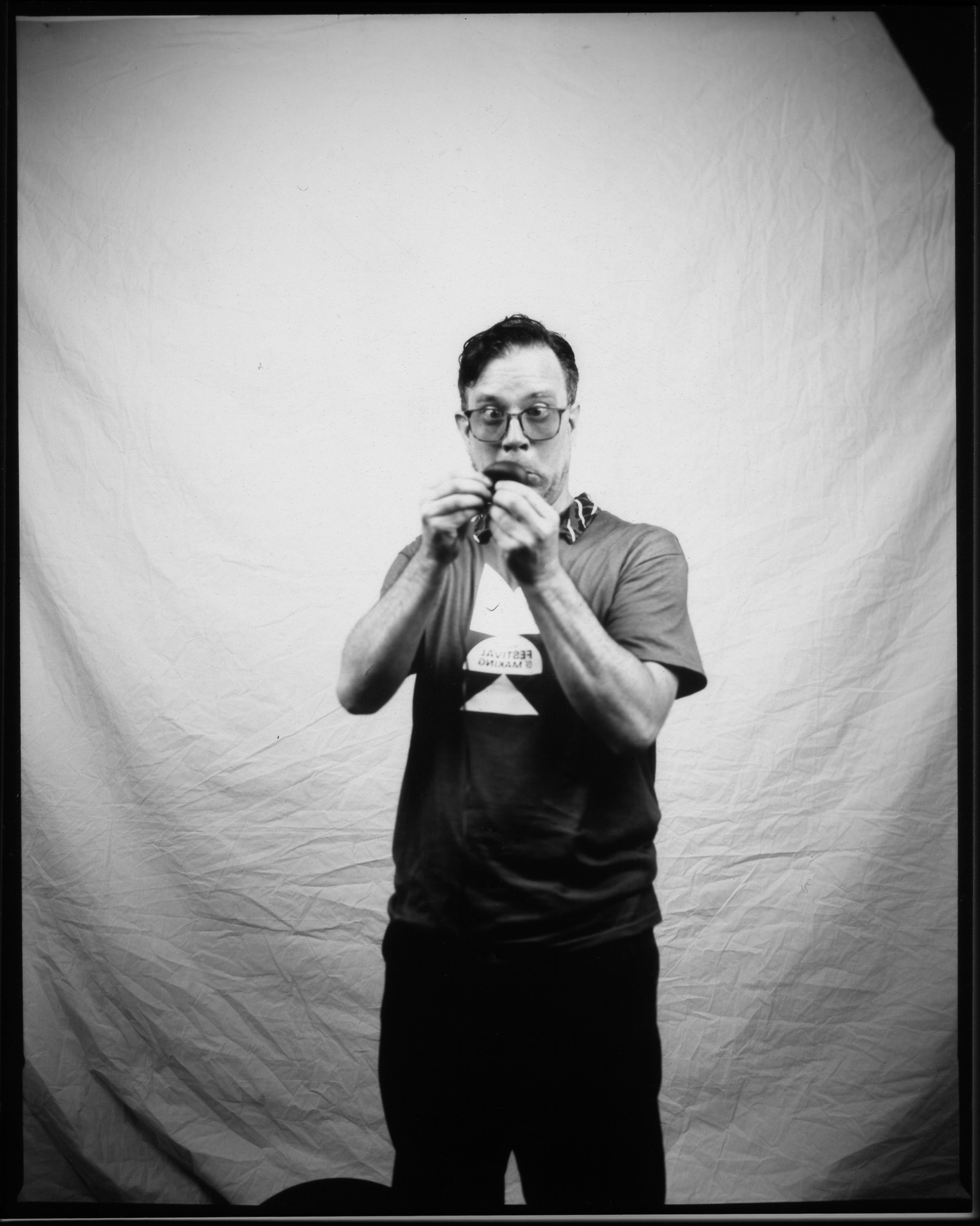 Adult with short hair and glasses, pulling a silly face while wearing a volunteer T-shirt and posing in a black and white photo.
