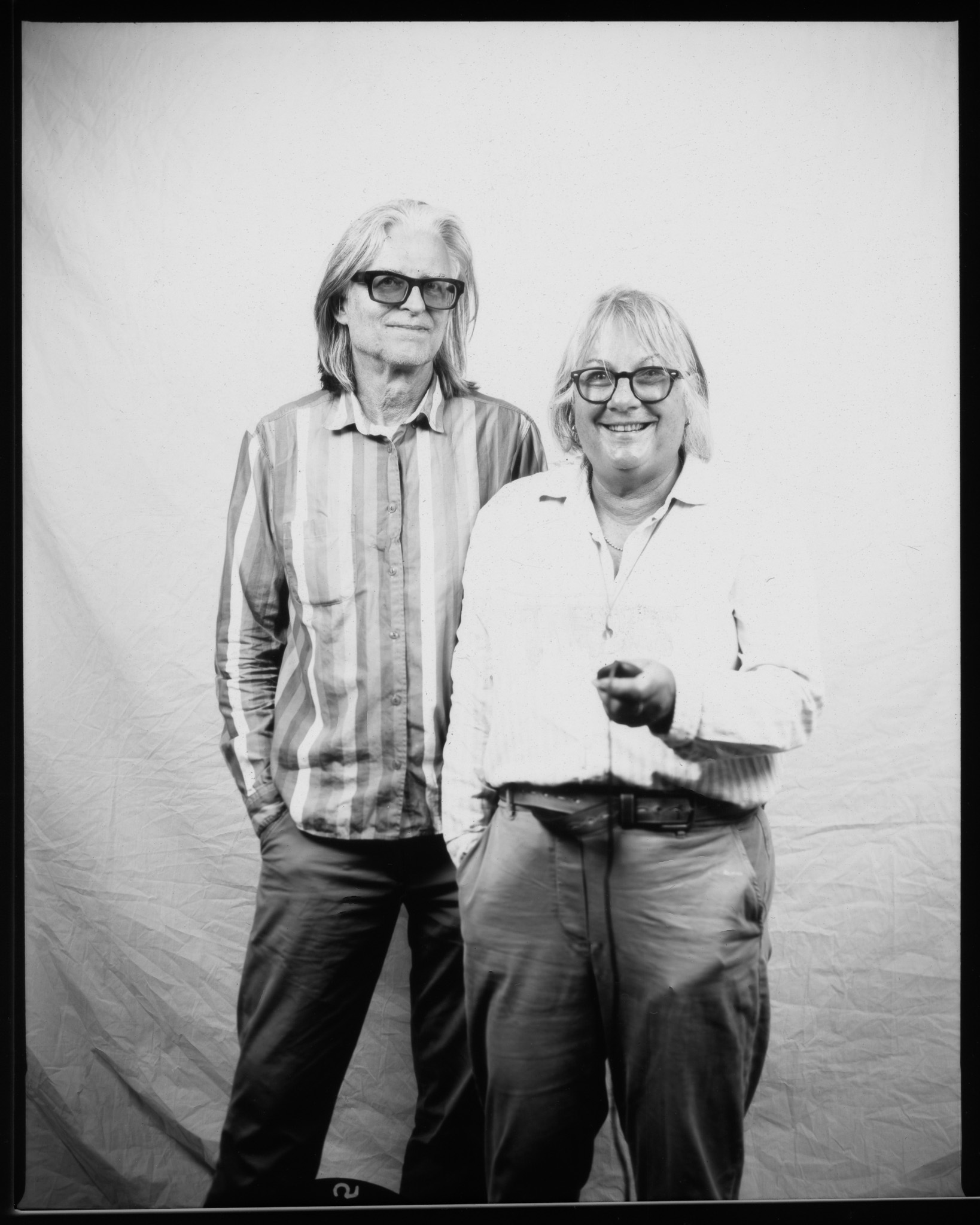 Two adults with mid-length hair smiling wearing glasses and shirts, posing in a black and white photo.