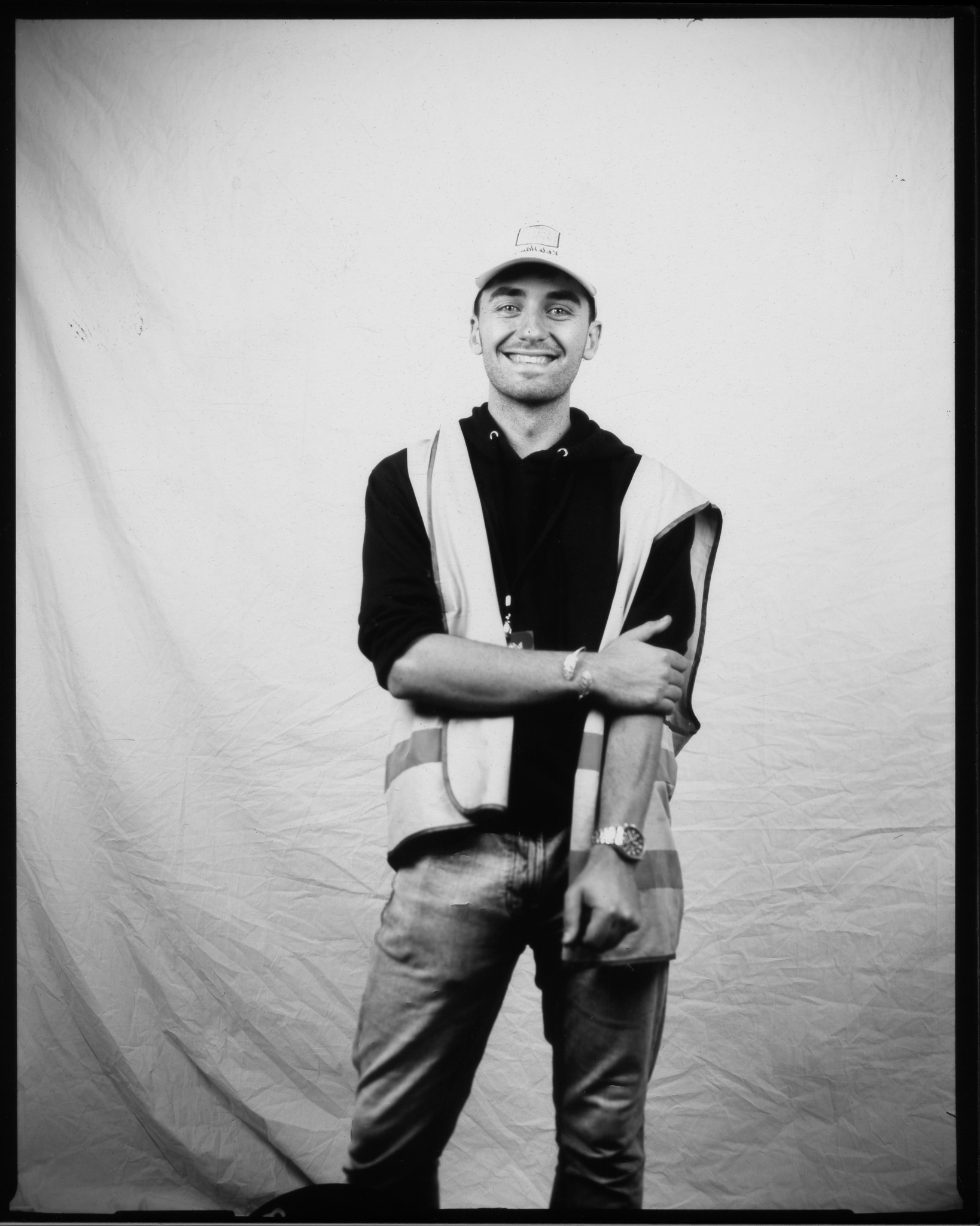 Adult wearing a high-vis vest and cap, smiling at the camera with one arm raised, posing in a black and white photo.