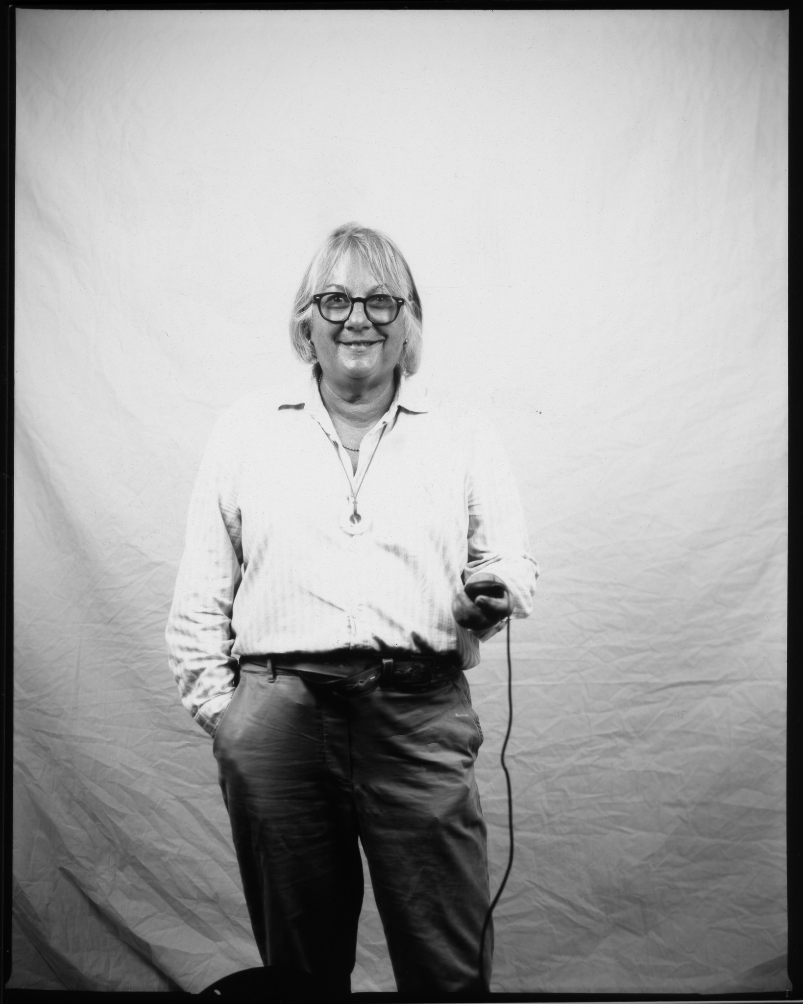 Smiling person in glasses and striped shirt holds a cable against a plain backdrop in a black and white photo.