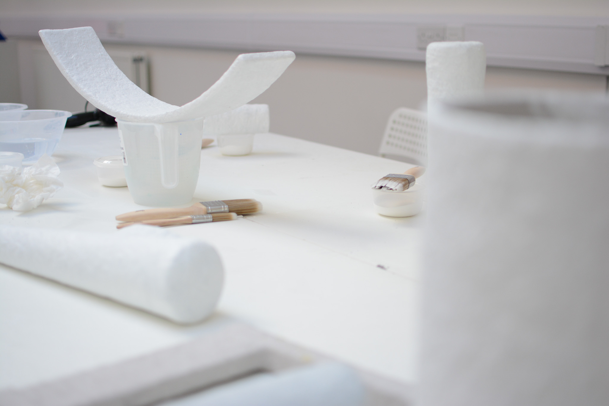 A bright, tidy workspace with sculptures, paintbrushes, and bowls on a white table.