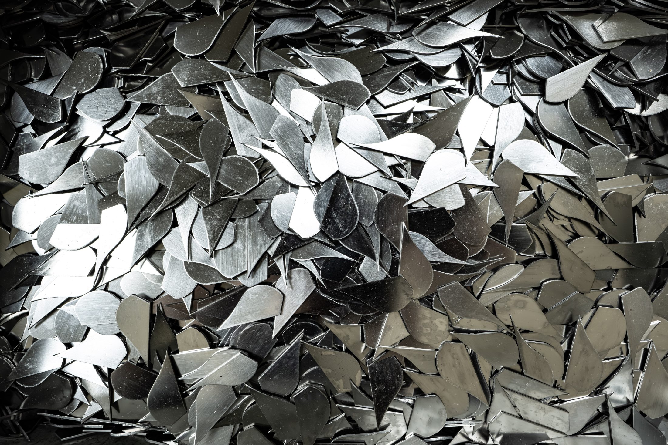 A large pile of shiny, flat metal pieces shaped like teardrops or leaves, overlapping each other and reflecting light.