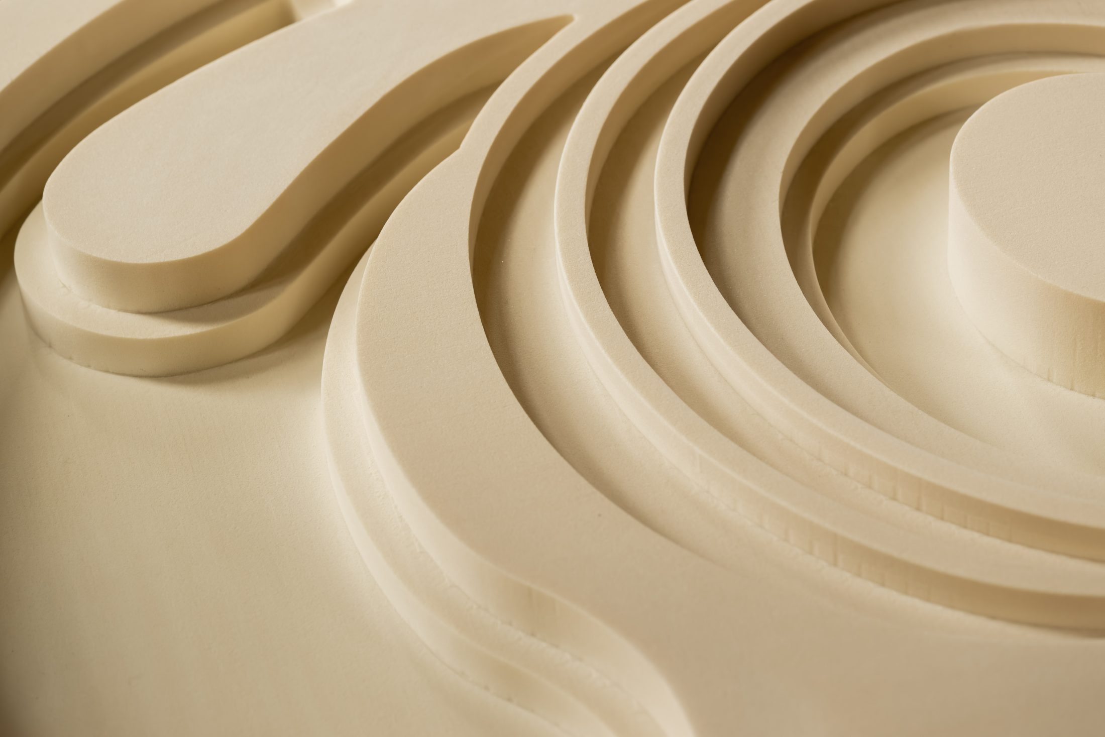 Close-up of a smooth, beige surface with layered, curved, and swirling patterns carved in relief, creating an abstract and three-dimensional appearance.