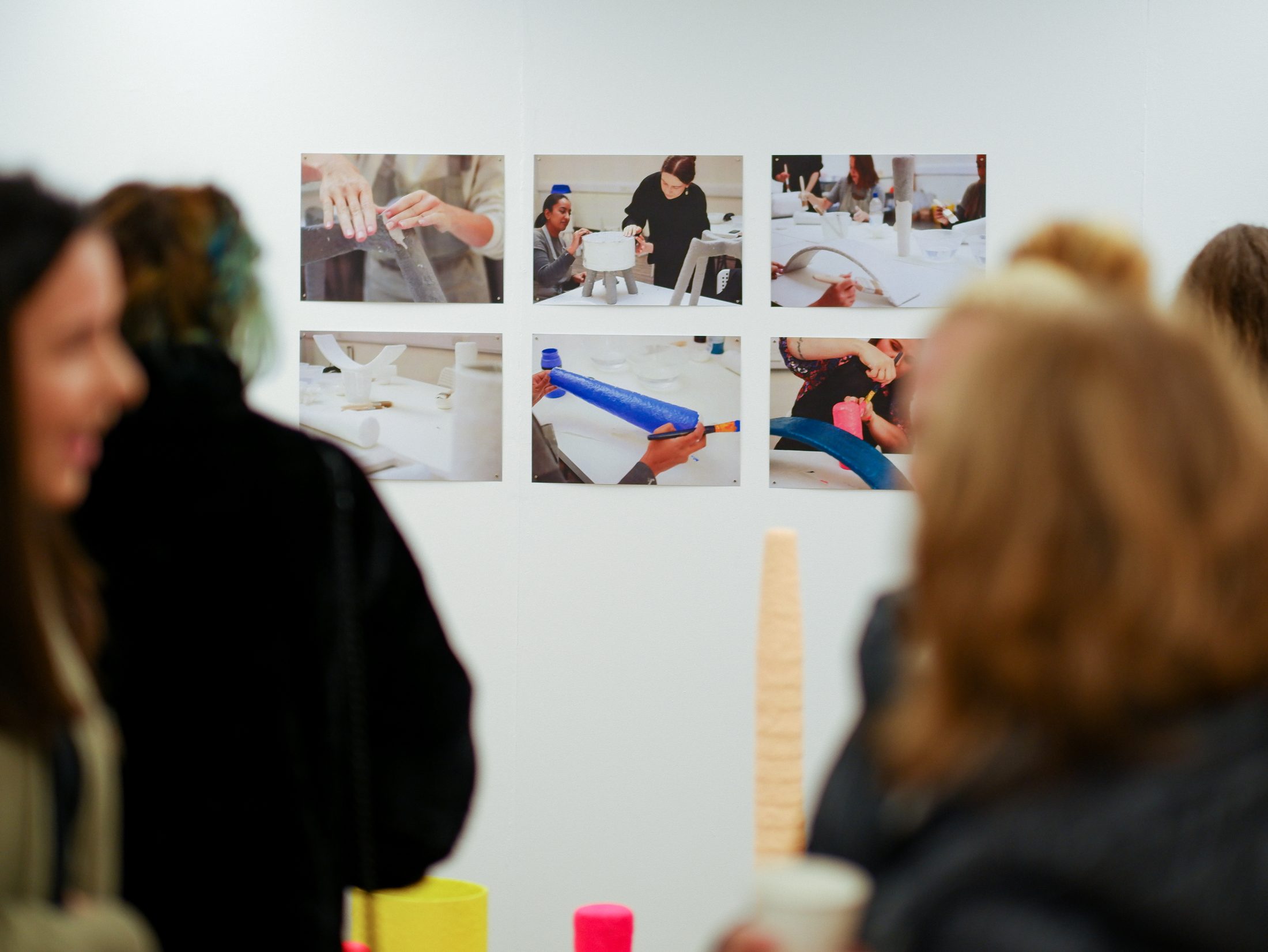 People view a gallery wall featuring six photos of hands crafting objects.